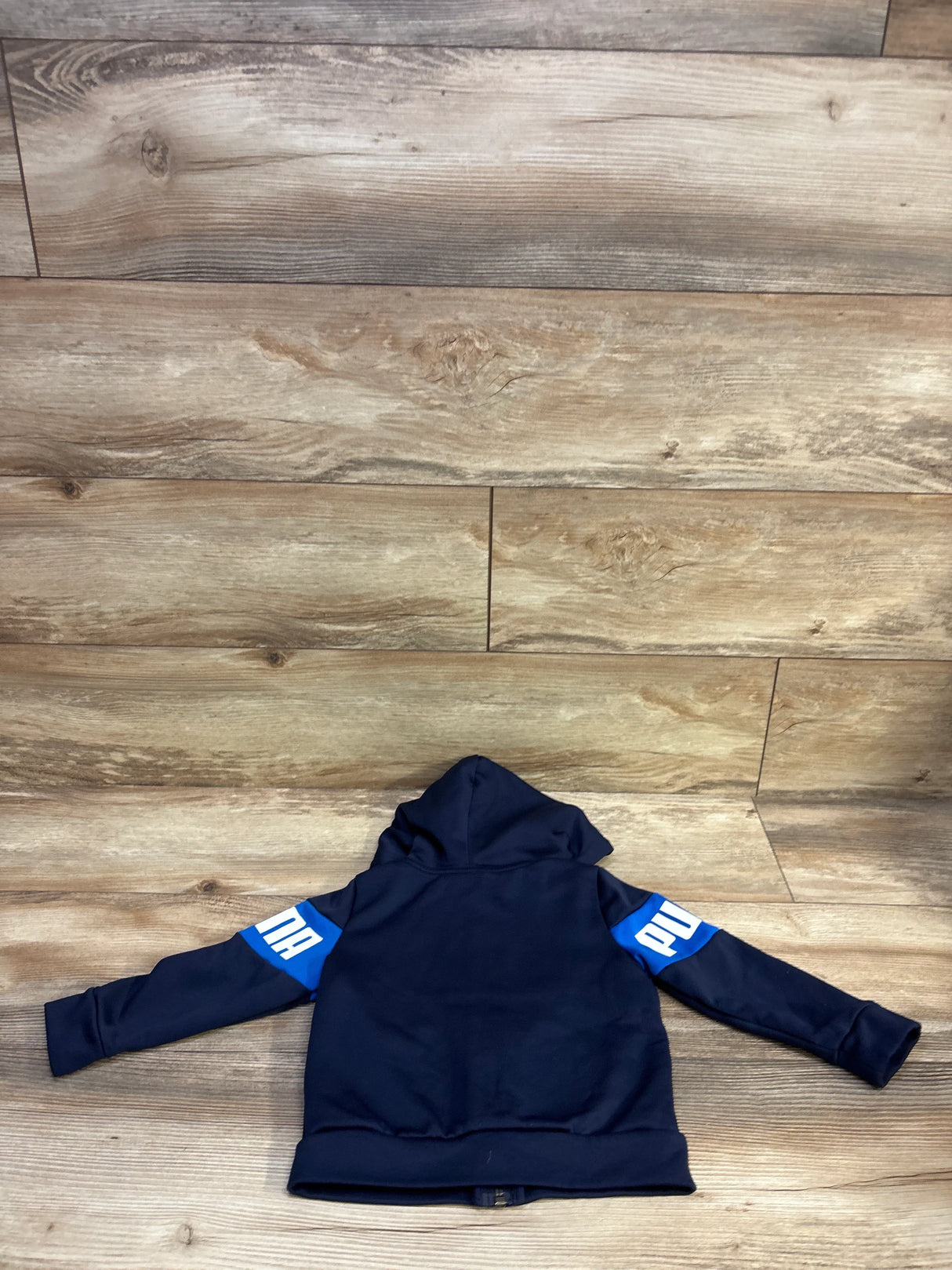 Back view of Puma toddler full-zip hooded jacket in navy blue with blue logo panels on sleeves on wood floor
