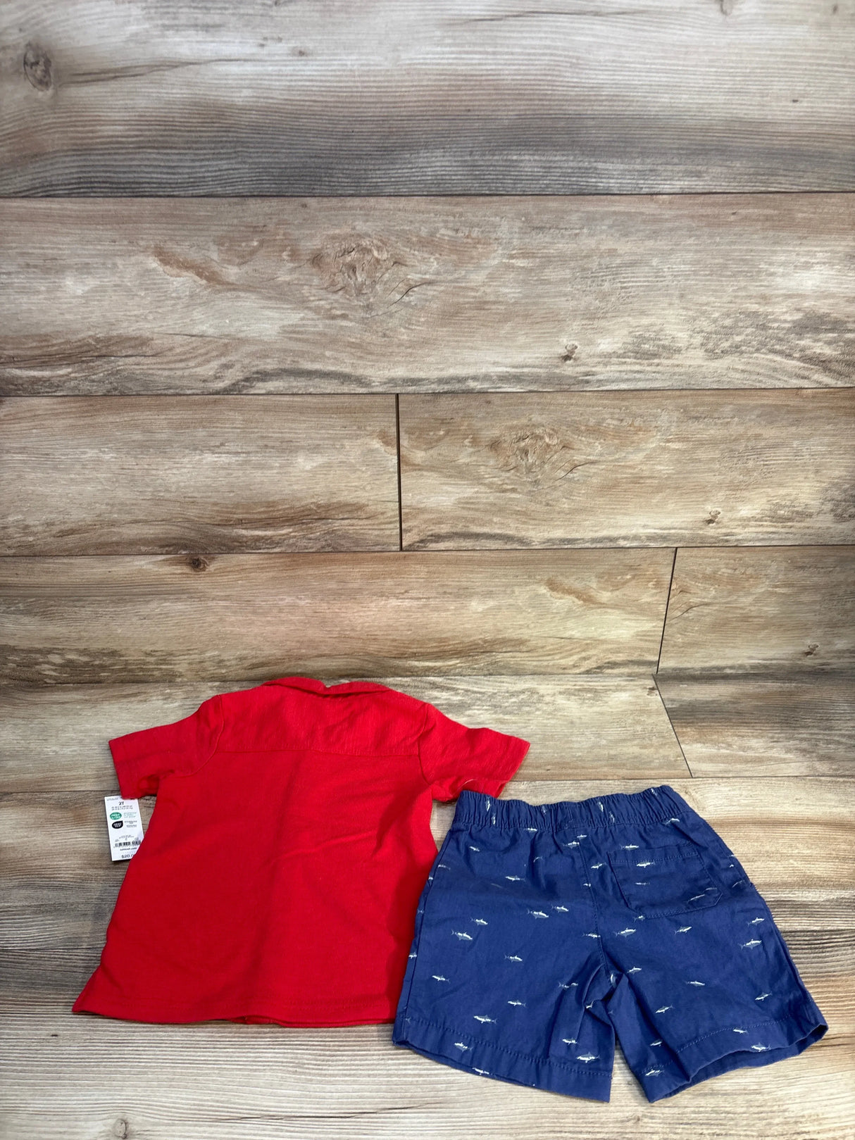 Red short sleeve toddler shirt and blue shorts with white shark print on wood background