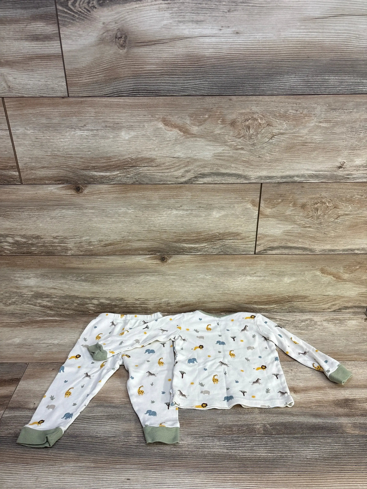 Top-down view of Mori Baby two-piece ivory safari pajama set (9–12 months) showing long-sleeve top and pants with green cuffs and animal print on wood background
