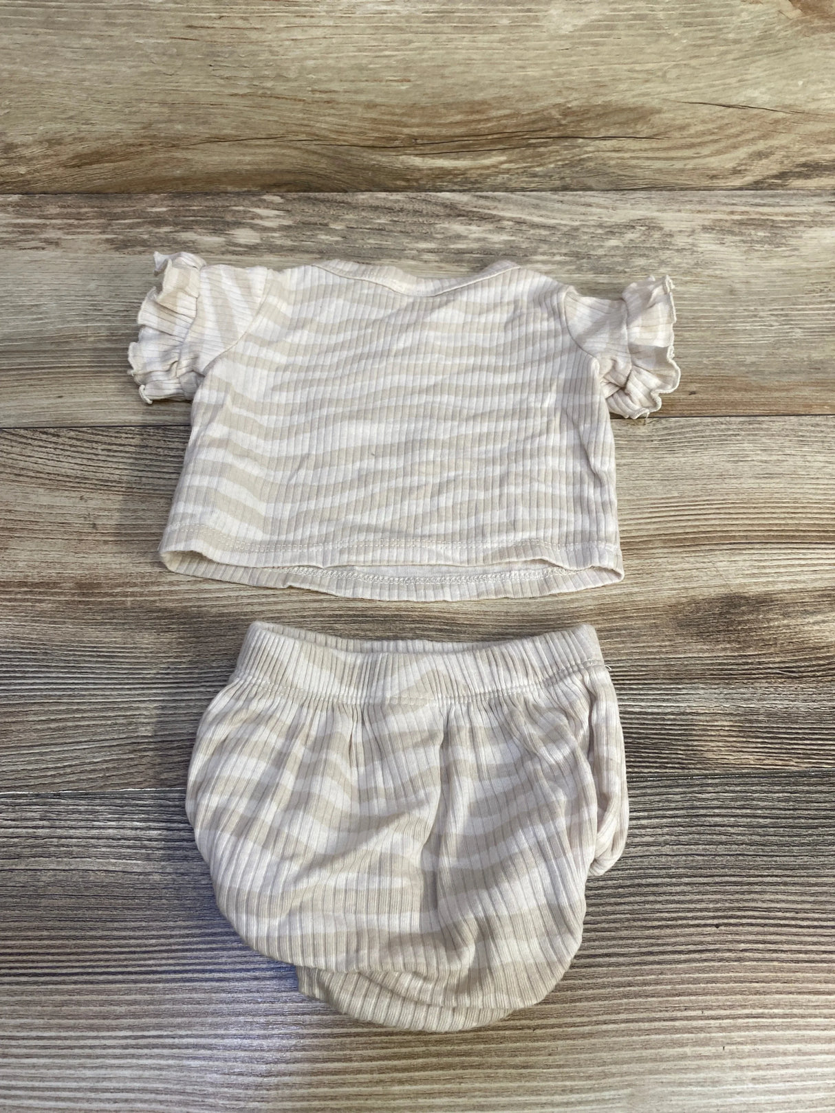 Flat lay of newborn ribbed two-piece shirt and bloomers showing ivory thin stripes and ruffled sleeves on wood background