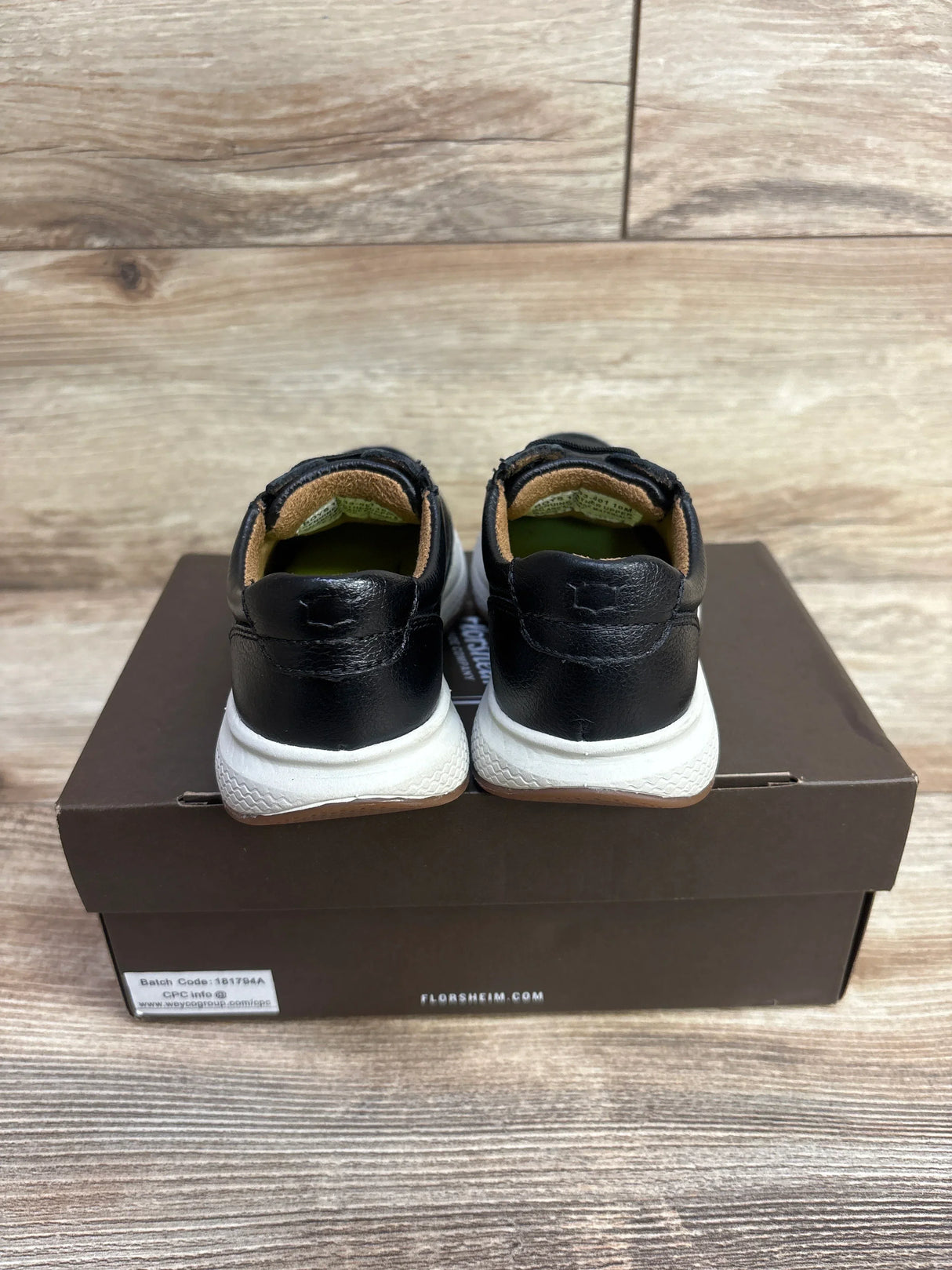 Rear view of black and white kids sneakers on a shoe box, wood background