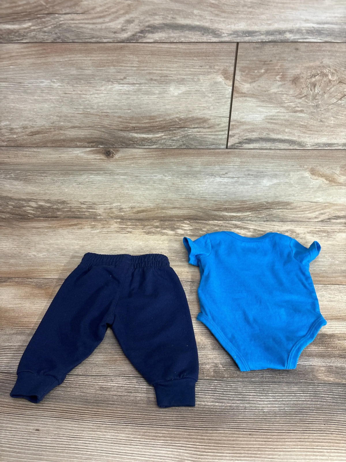 Flat lay of Hurley 2-piece baby set: blue short-sleeve onesie and navy elastic-waist pants on wood floor