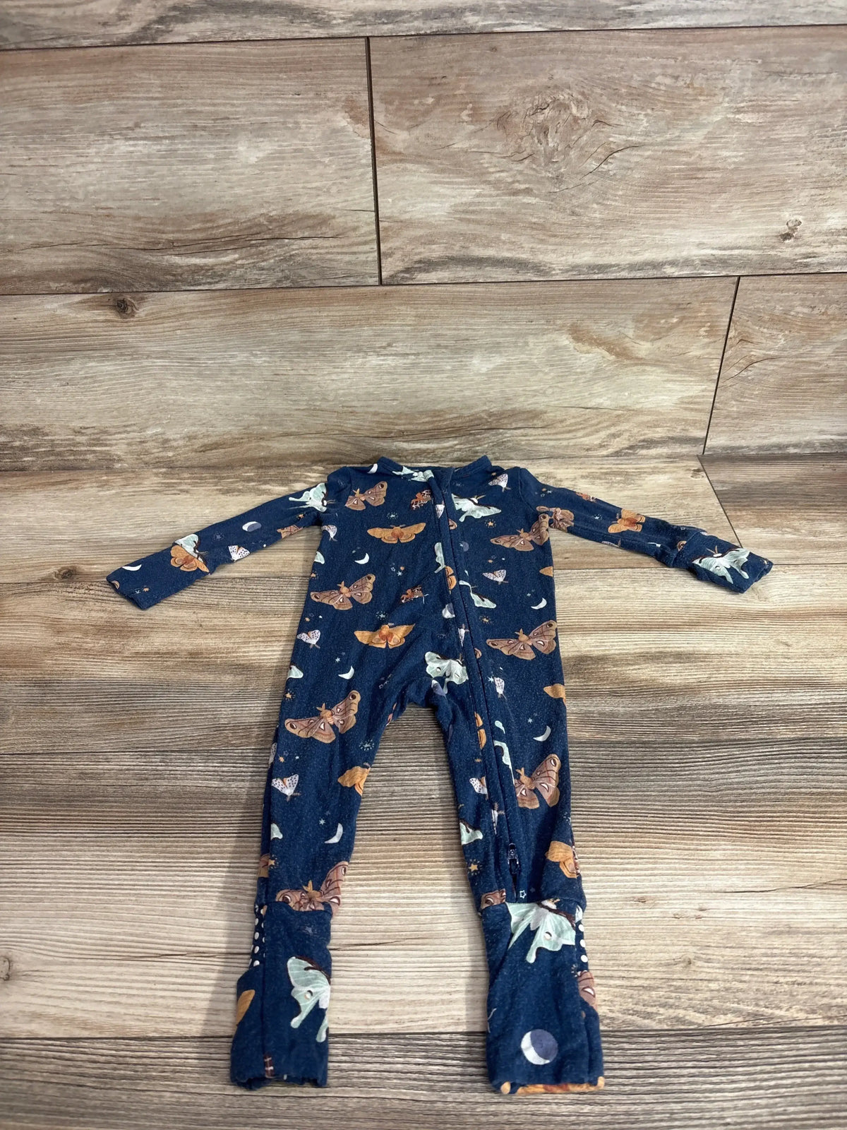 Flat lay of Angel Dear navy bamboo butterfly convertible zip sleeper showcasing front zipper and moth print on wood floor