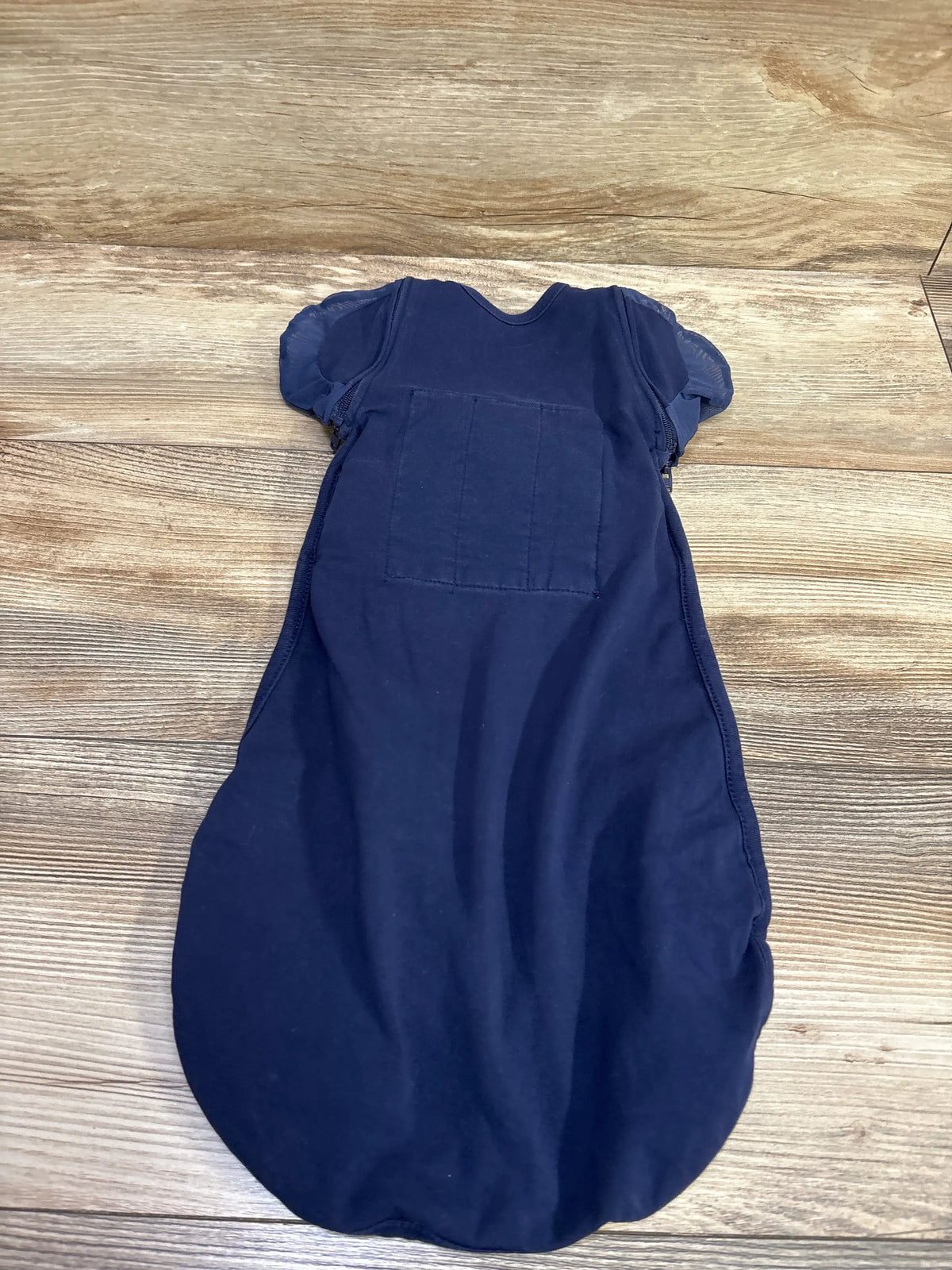Front view of Nested Bean Zen One Classic Convertible Swaddle in navy showing short sleeves and chest panel on wood grain