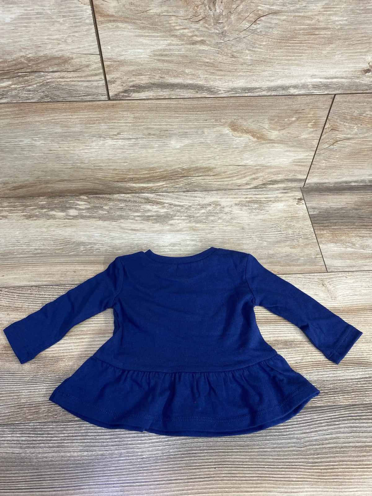 Navy blue long-sleeve baby top with peplum hem laid flat on wood floor background