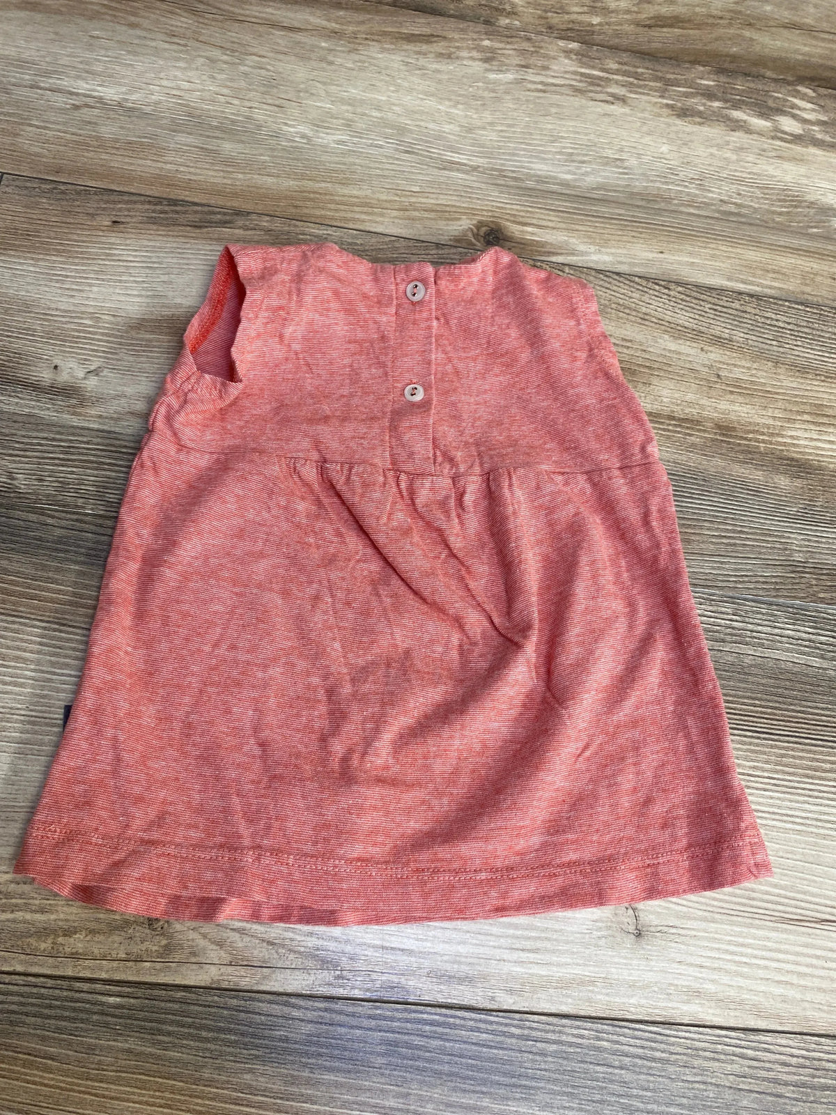 Flat-lay of red heathered sleeveless baby dress showing back button closure and gathered waist on wood floor background