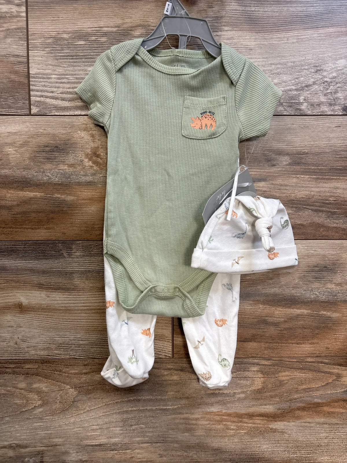 Front view of green ribbed baby bodysuit with matching white footed pants and knotted hat with dinosaur prints