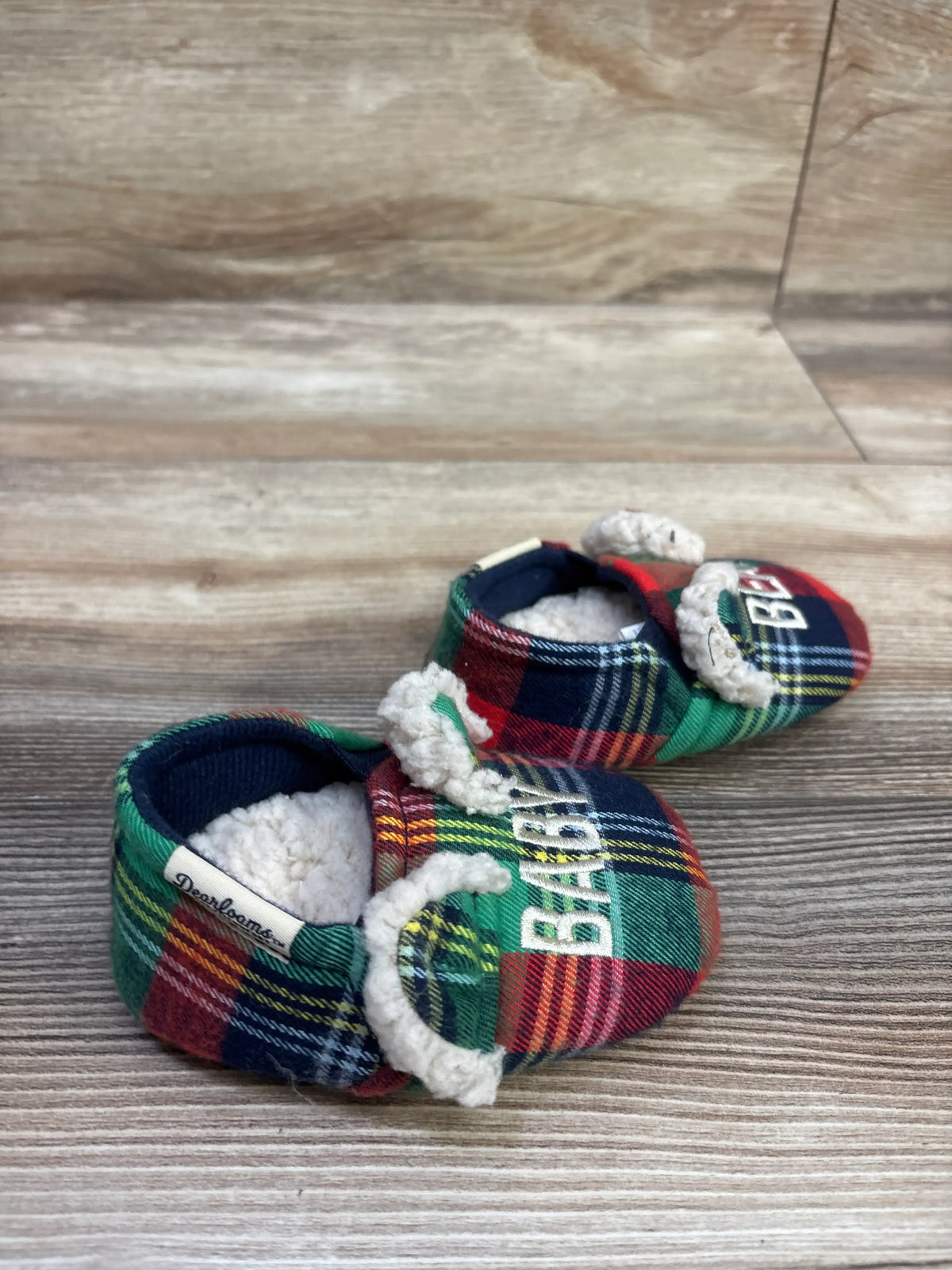 Close-up of Dearfoams baby bear slippers in size 4C showcasing multicolor plaid fabric and fuzzy lining on a wood surface