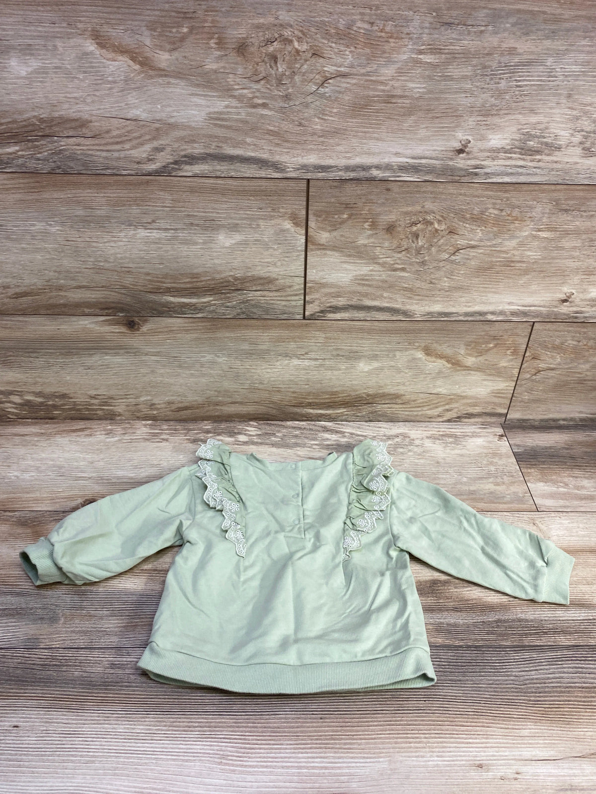 Front view of green Little Me eyelet sweatshirt showcasing ruffled eyelet trim with a wood backdrop