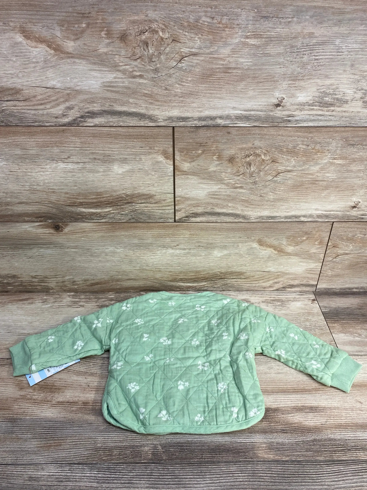 back view of green quilted baby jacket with white floral print on wooden floor
