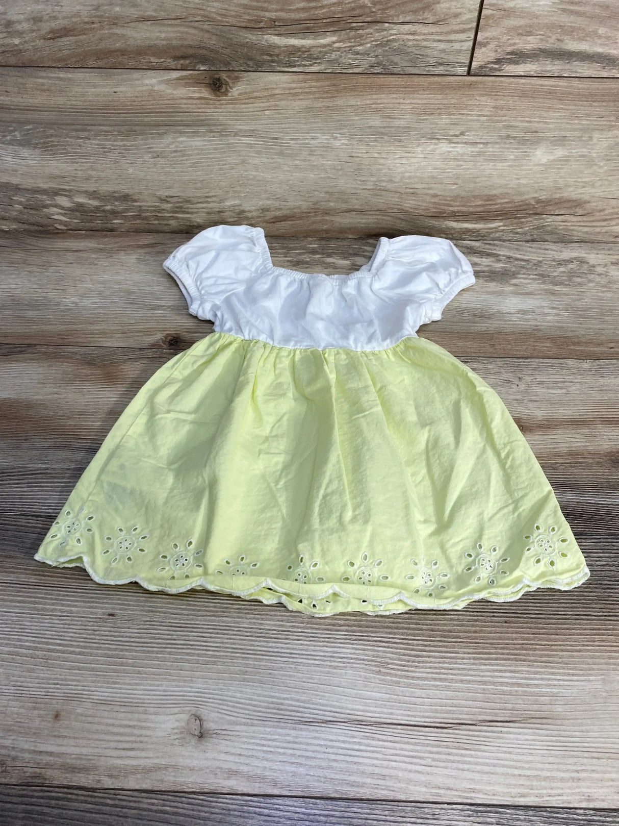 Flat lay of Baby Gap poplin eyelet dress with white puff sleeves and pale yellow eyelet skirt with scalloped hem on wood background