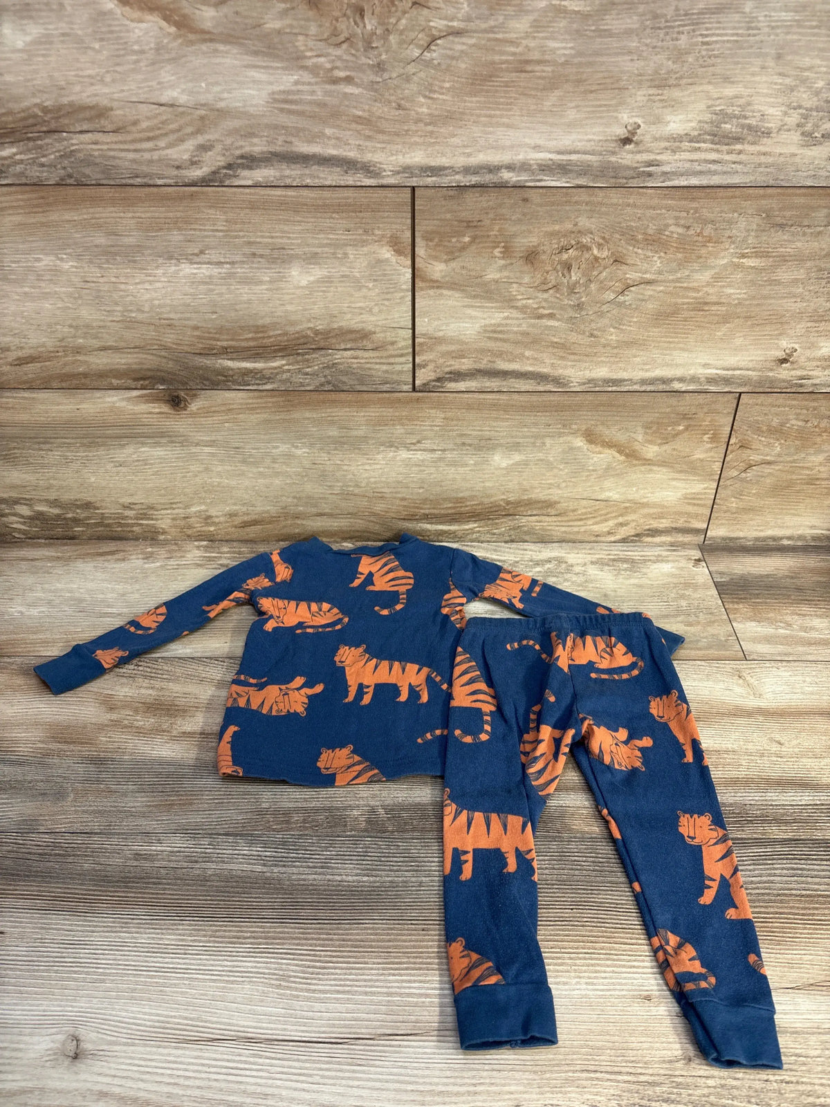 Just One You blue 2-piece baby pajama set with orange tiger print on a wooden background