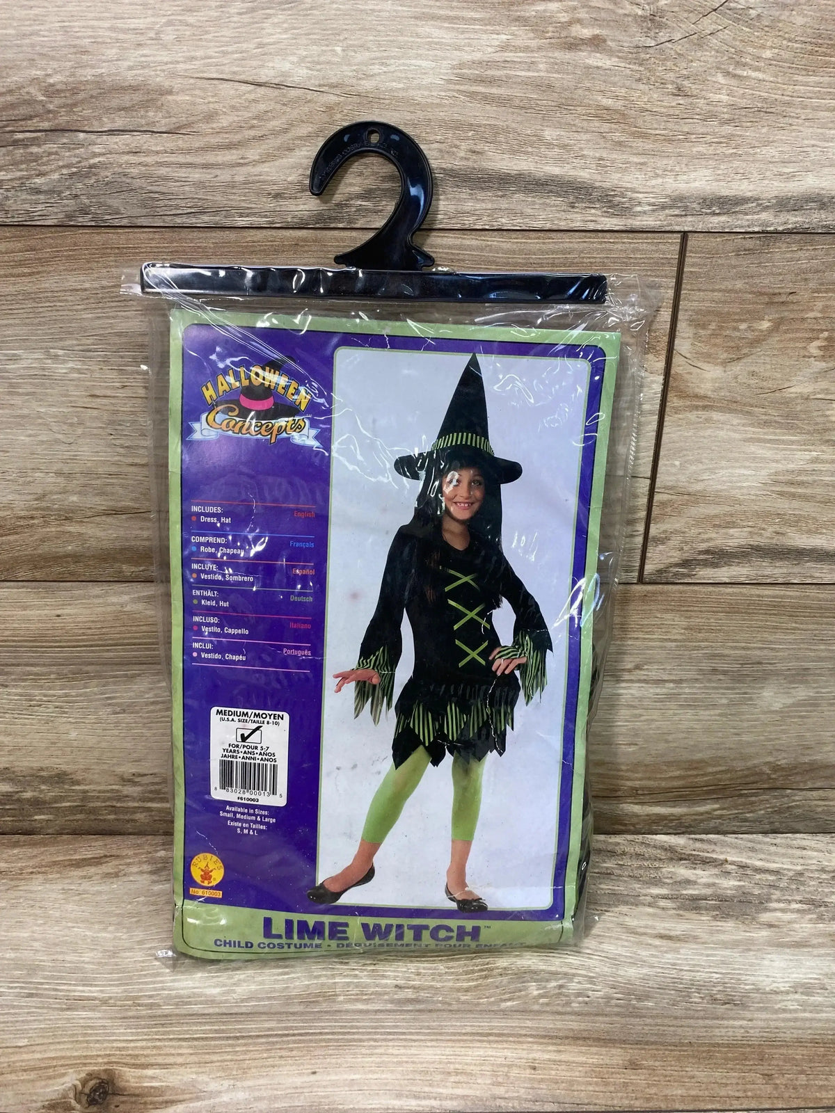 Packaged front view of Lime Witch costume size 8-10 showing black dress with lime-green trim, green leggings and pointed hat on wooden background