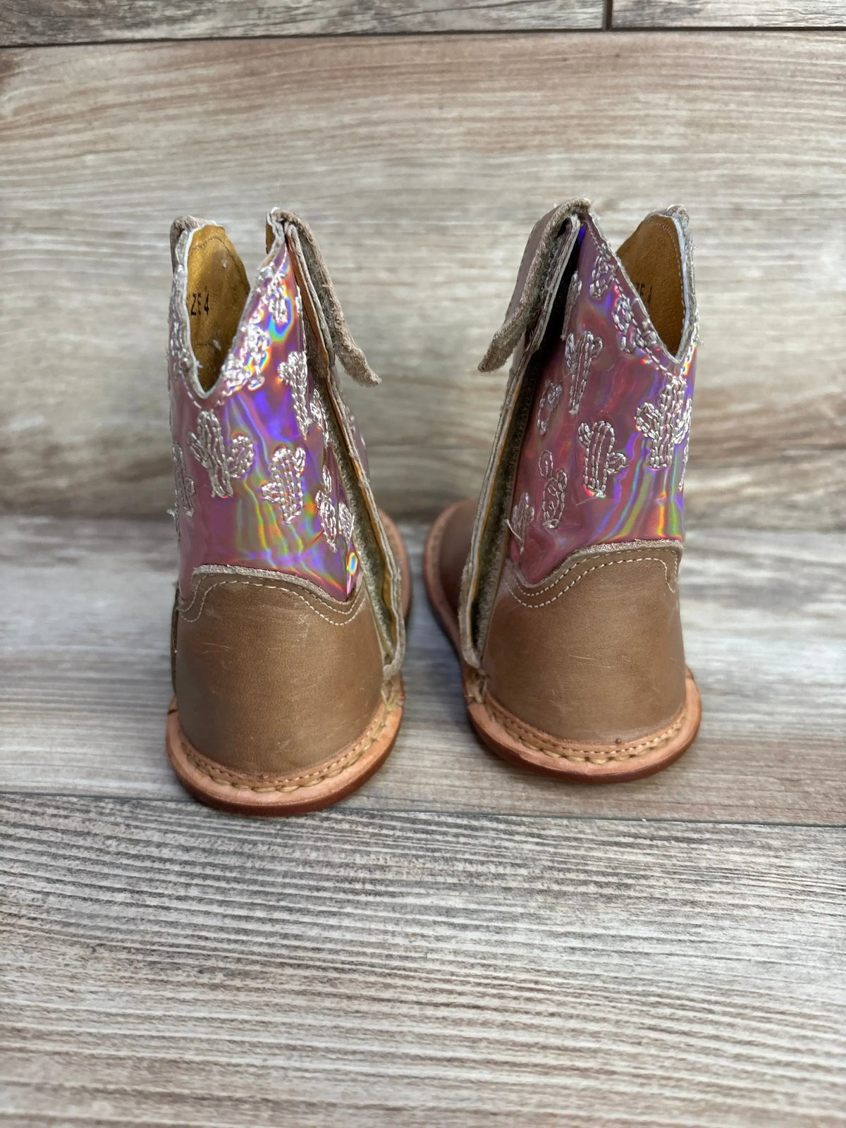 Rear view of kids pink iridescent Roper cowgirl boots showing cactus embroidery and brown leather heel on wood background