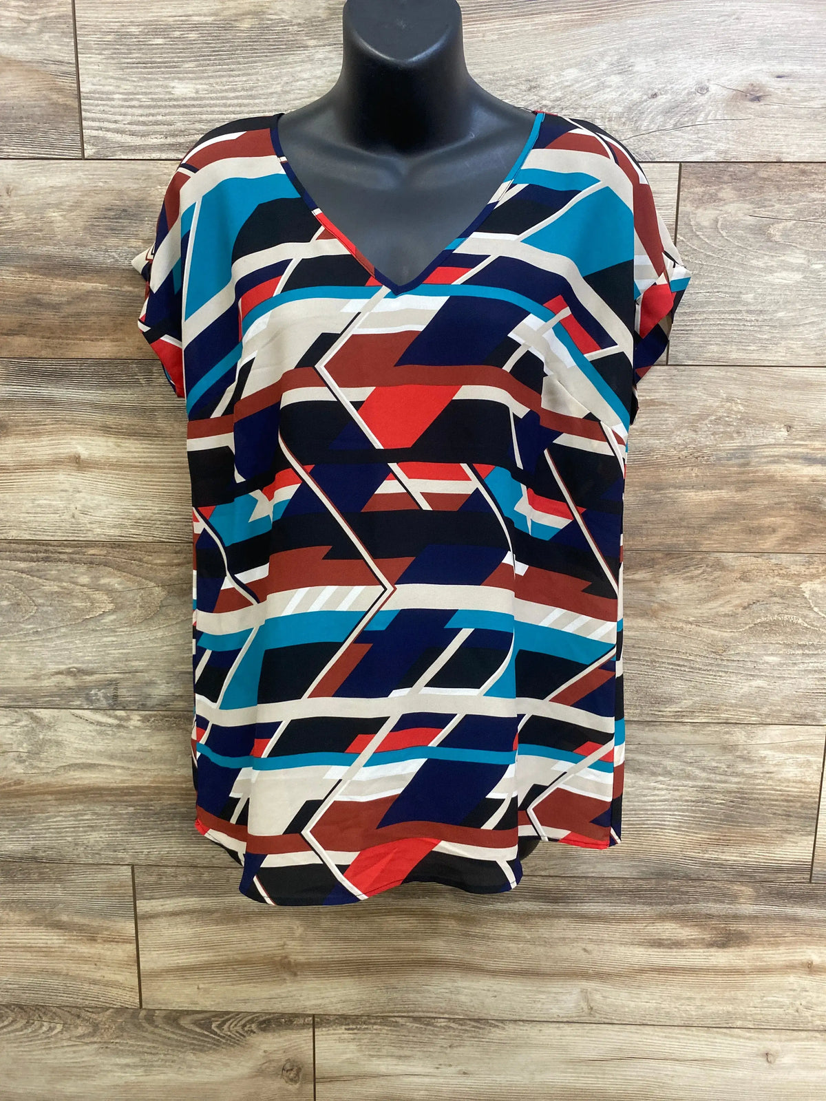 Front view of Motherhood Maternity v-neck shirt showcasing geometric multicolor pattern and relaxed fit on a wood floor background