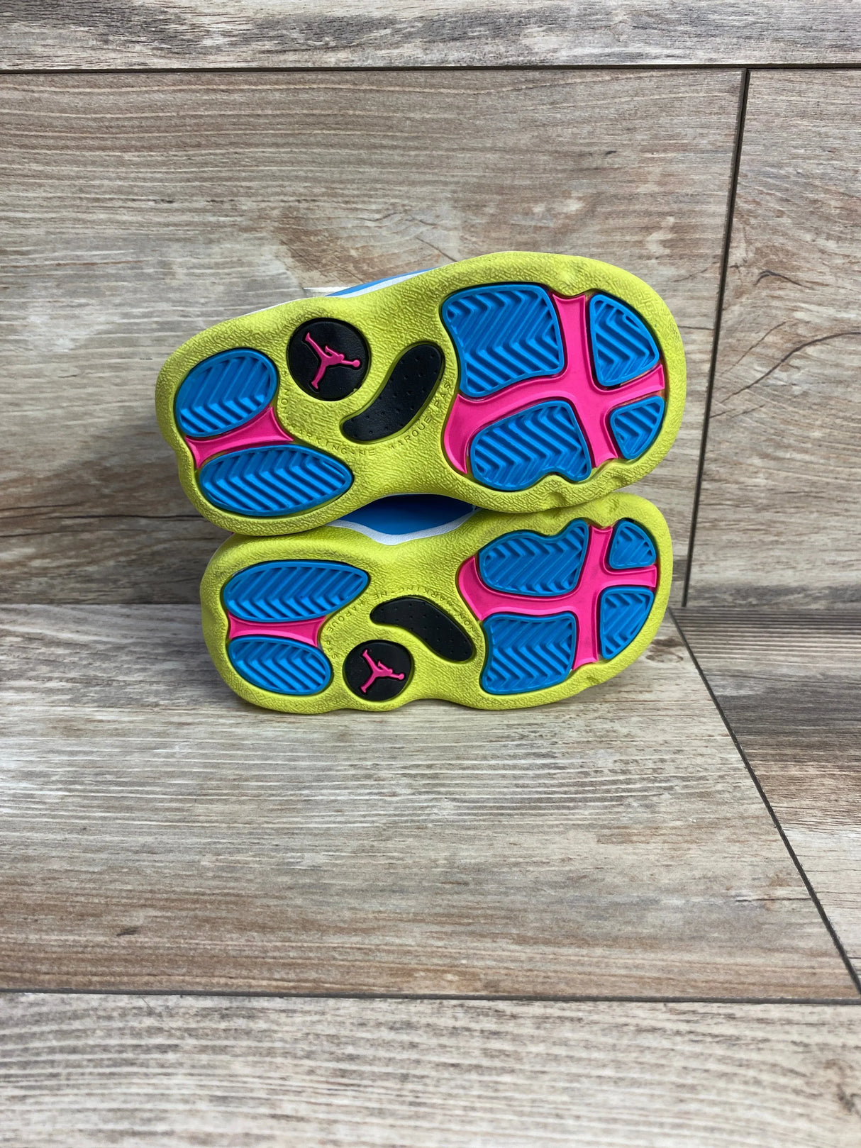 Bottom view of Air Jordan 6 Rings TD toddler sneakers (size 5C) showing neon yellow soles with blue and pink accents on wood floor
