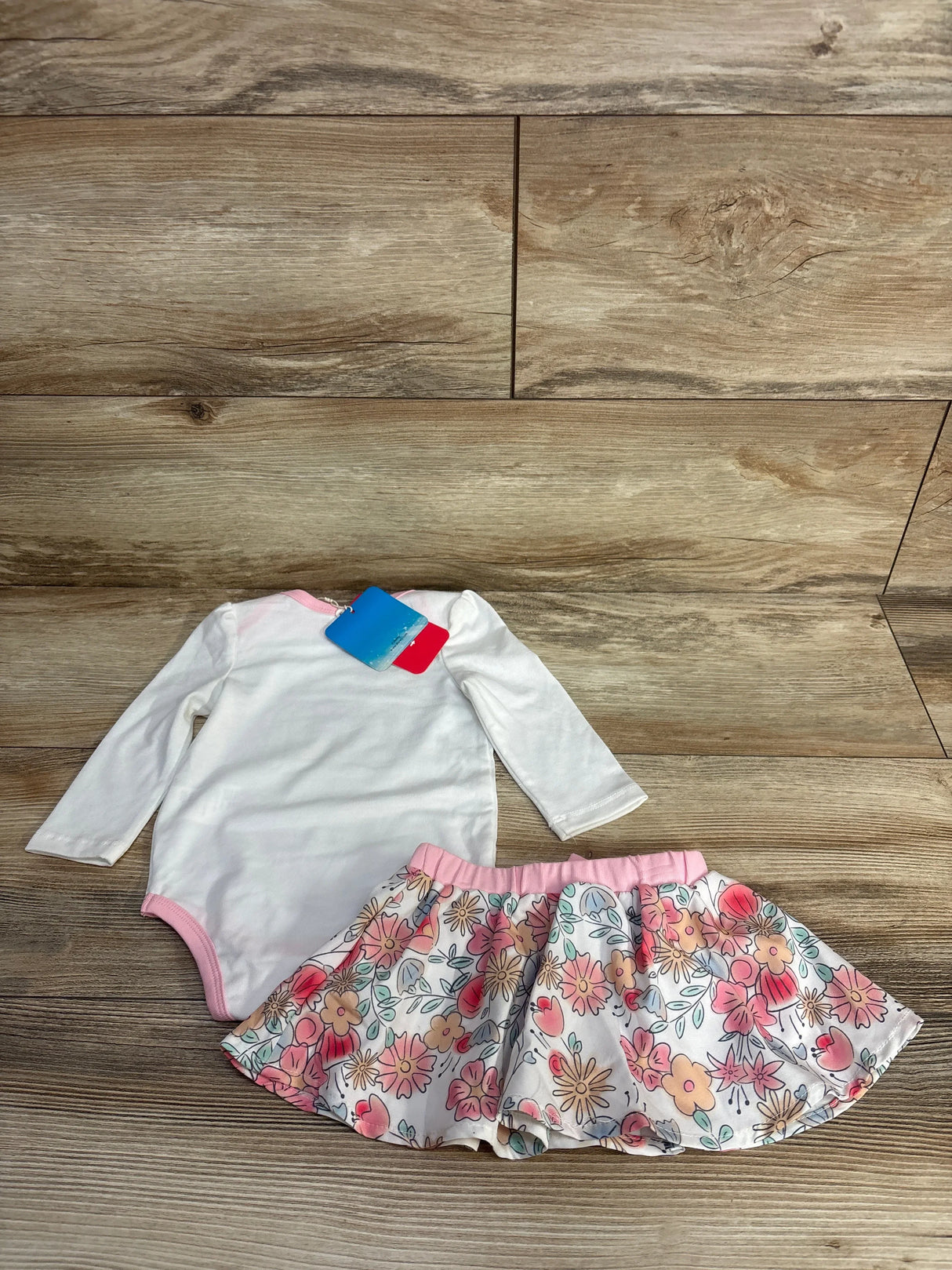 Baby girls' white long sleeve bodysuit and floral skirt set on wooden floor