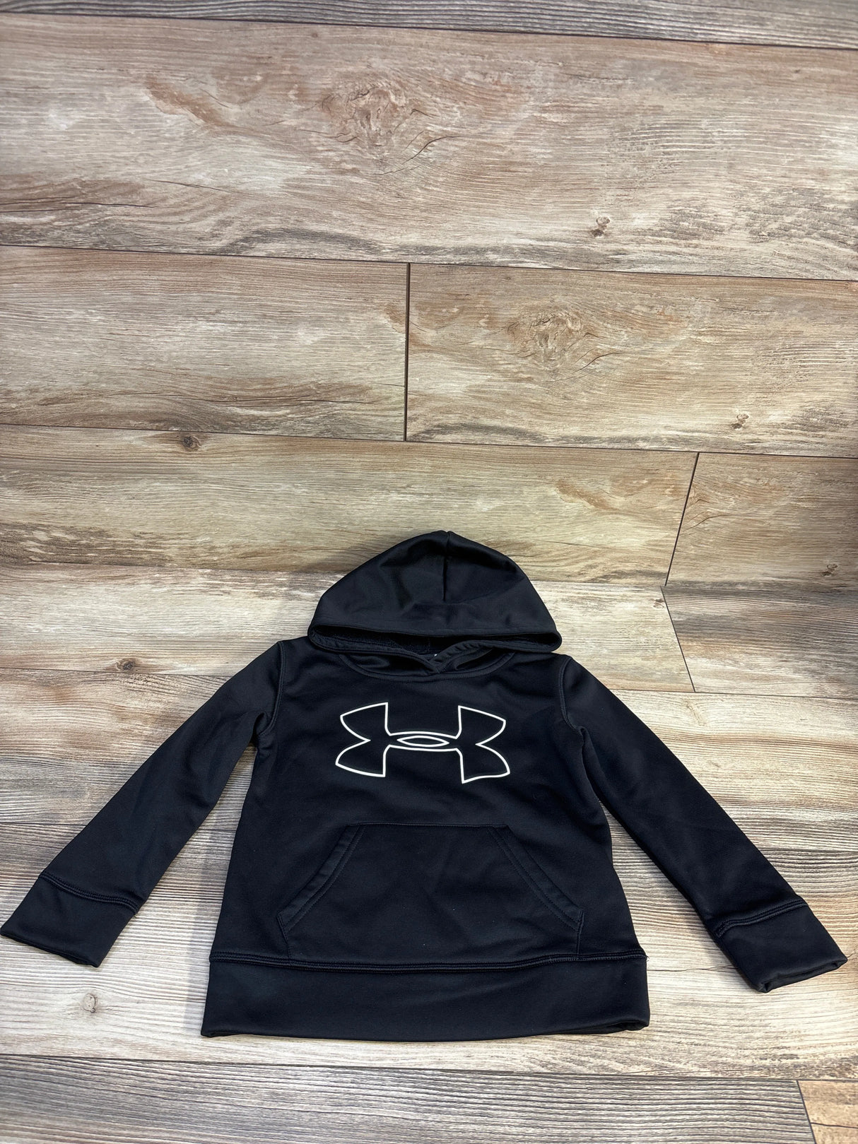 Front view of black Under Armour pullover hooded sweatshirt in size 4T showcasing kangaroo pocket and logo on a wood floor