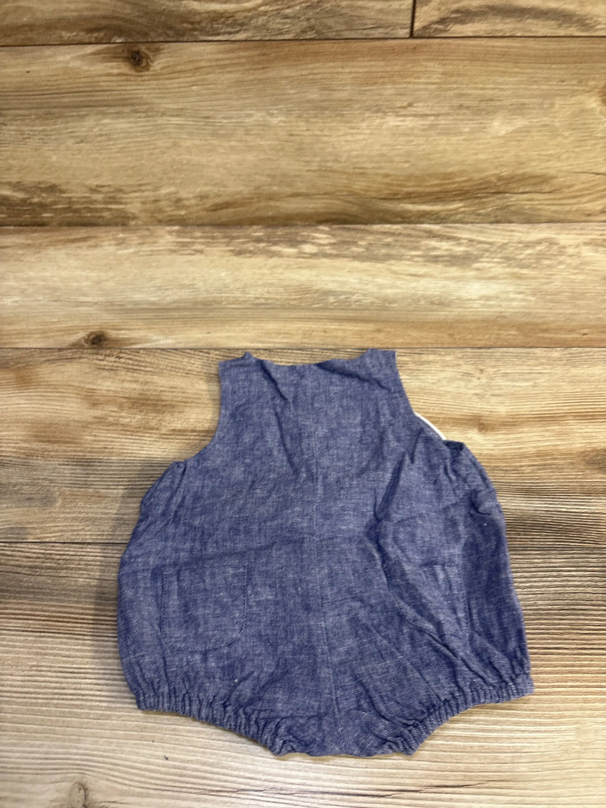 Top-down view of chambray bubble romper showing sleeveless style, elastic leg openings and front pocket on wood surface
