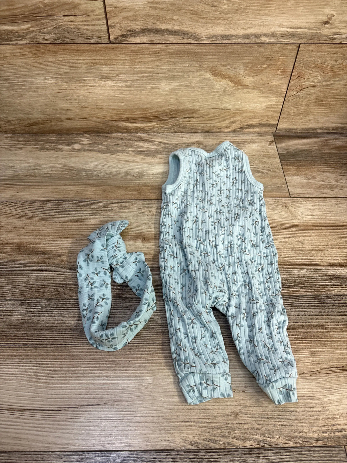 Top view of the blue ribbed jumpsuit and matching headband set showcasing the botanical print with a wood floor background