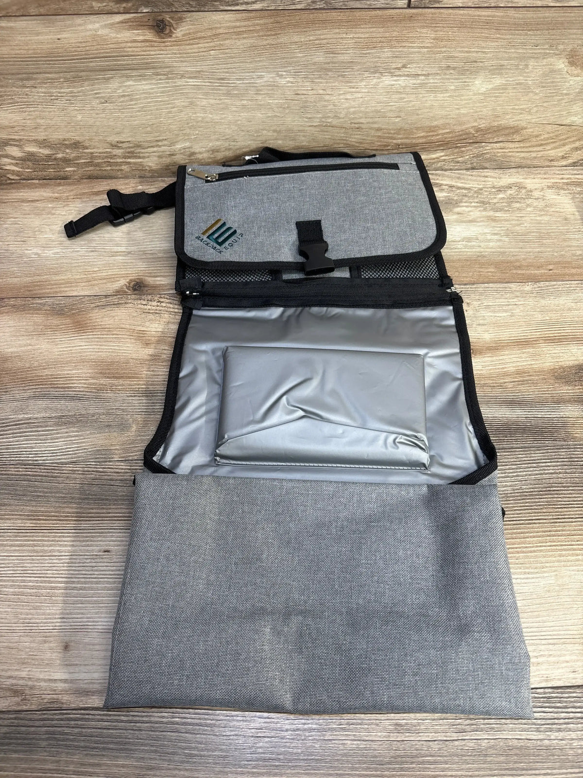 Open view of NEW Backpack Equip Portable Changing Station Grey showcasing silver changing pad and zippered pockets on wood