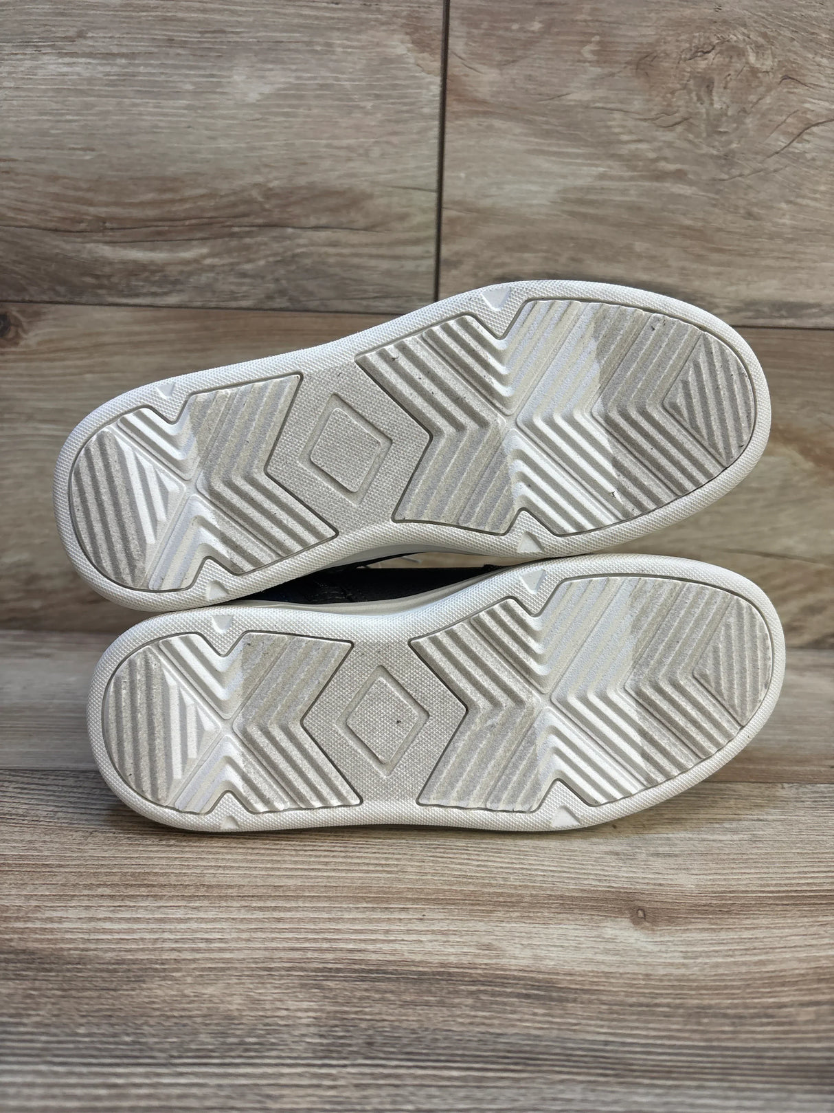 Kids' sneakers with white rubber soles, showing lightly worn tread on wood floor