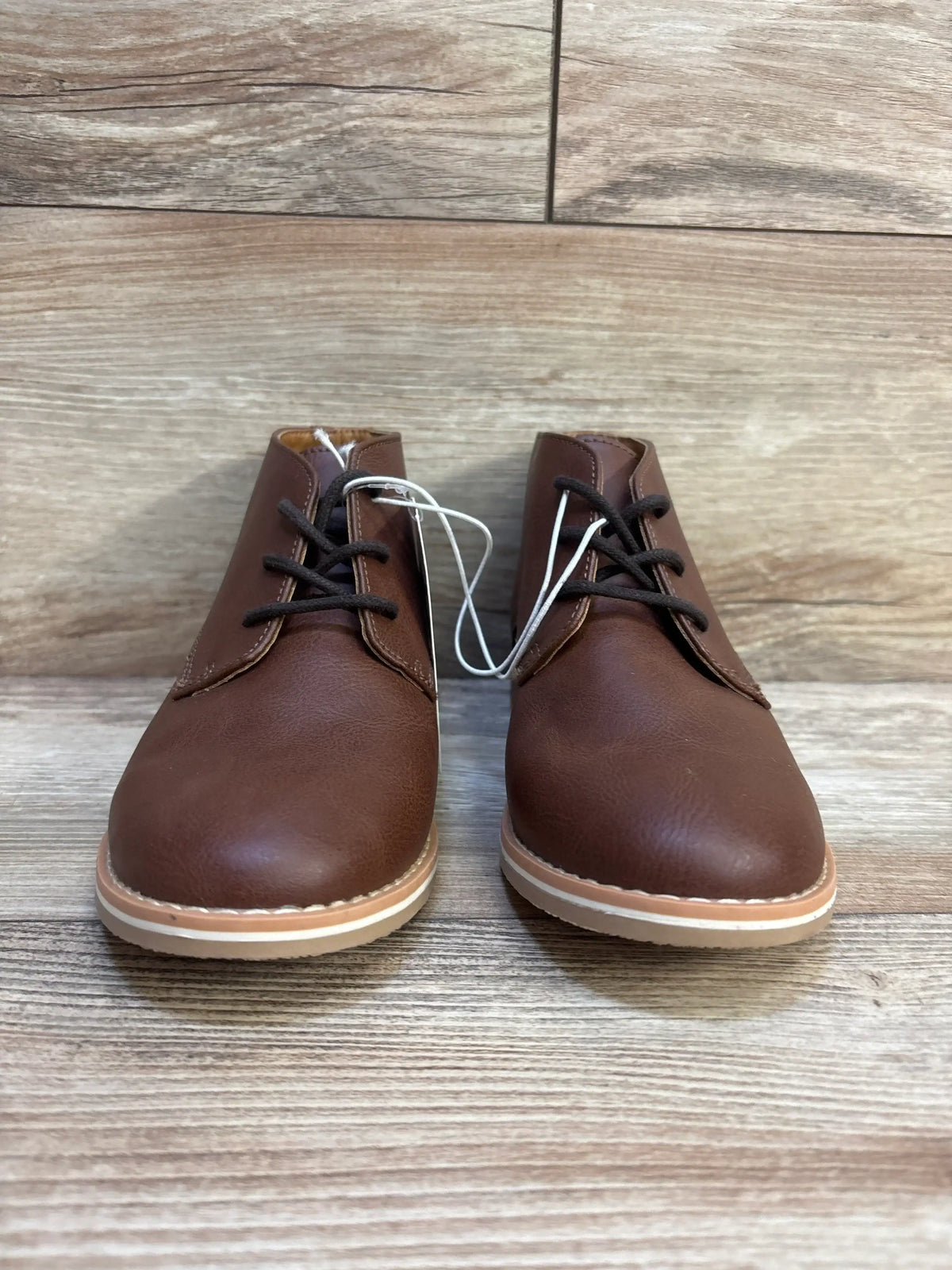 Brown leather kids lace-up shoes with rubber soles on wood background