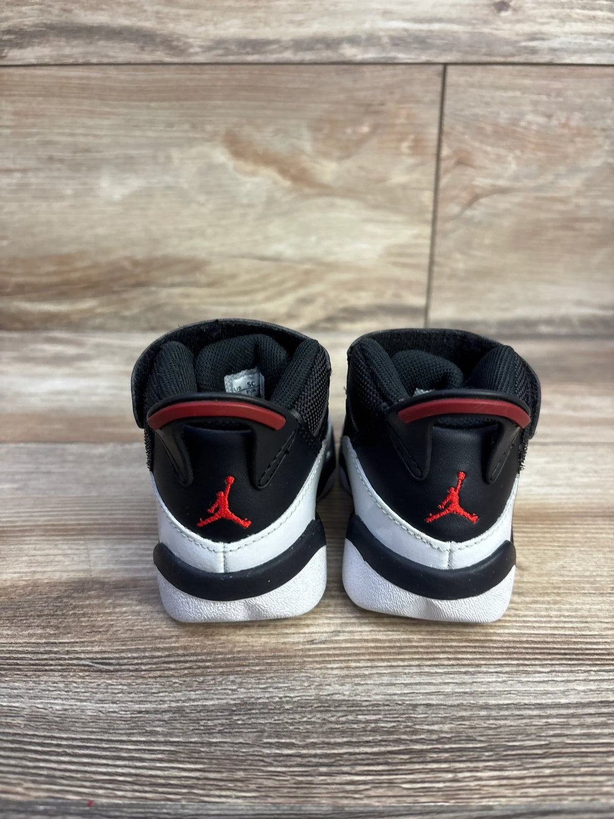 Rear view of Air Jordan 6 Rings toddler sneakers showing red Jumpman on black-and-white heel, padded collar on wood floor