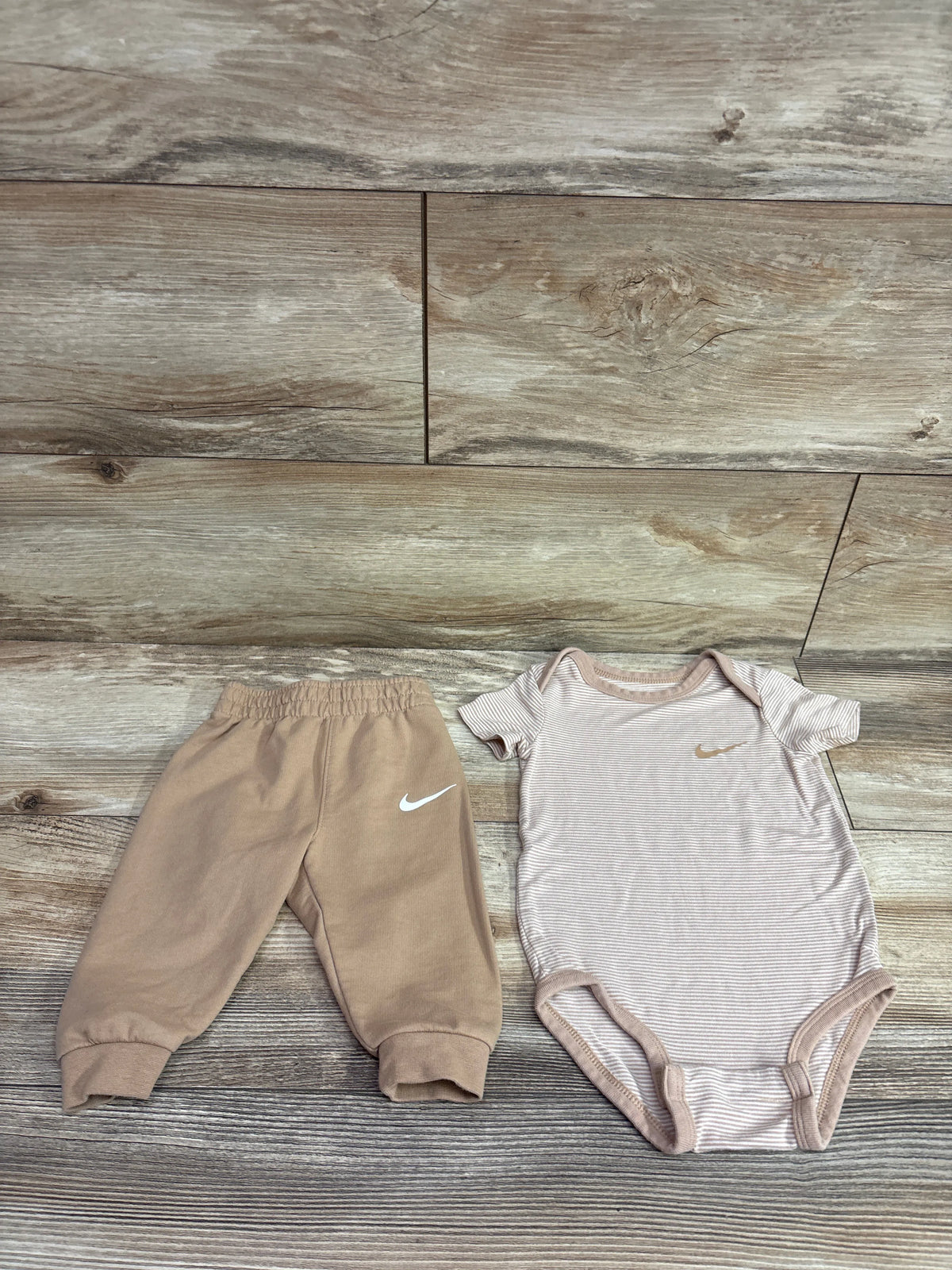 Nike 2pc tan viscose bodysuit and joggers set for infants on a wooden background