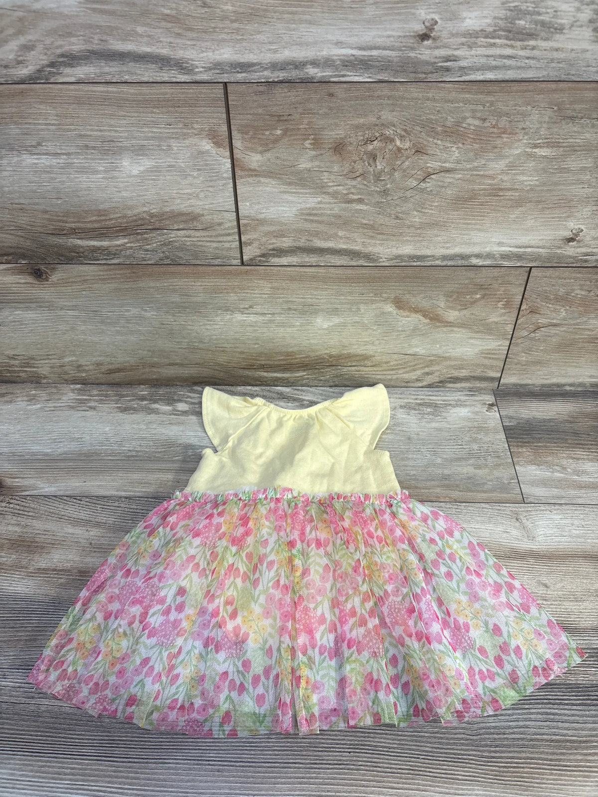 Front view of Kids Headquarters floral tulle overlay dress in yellow, with cap sleeves and Let Love Bloom text on wood floor