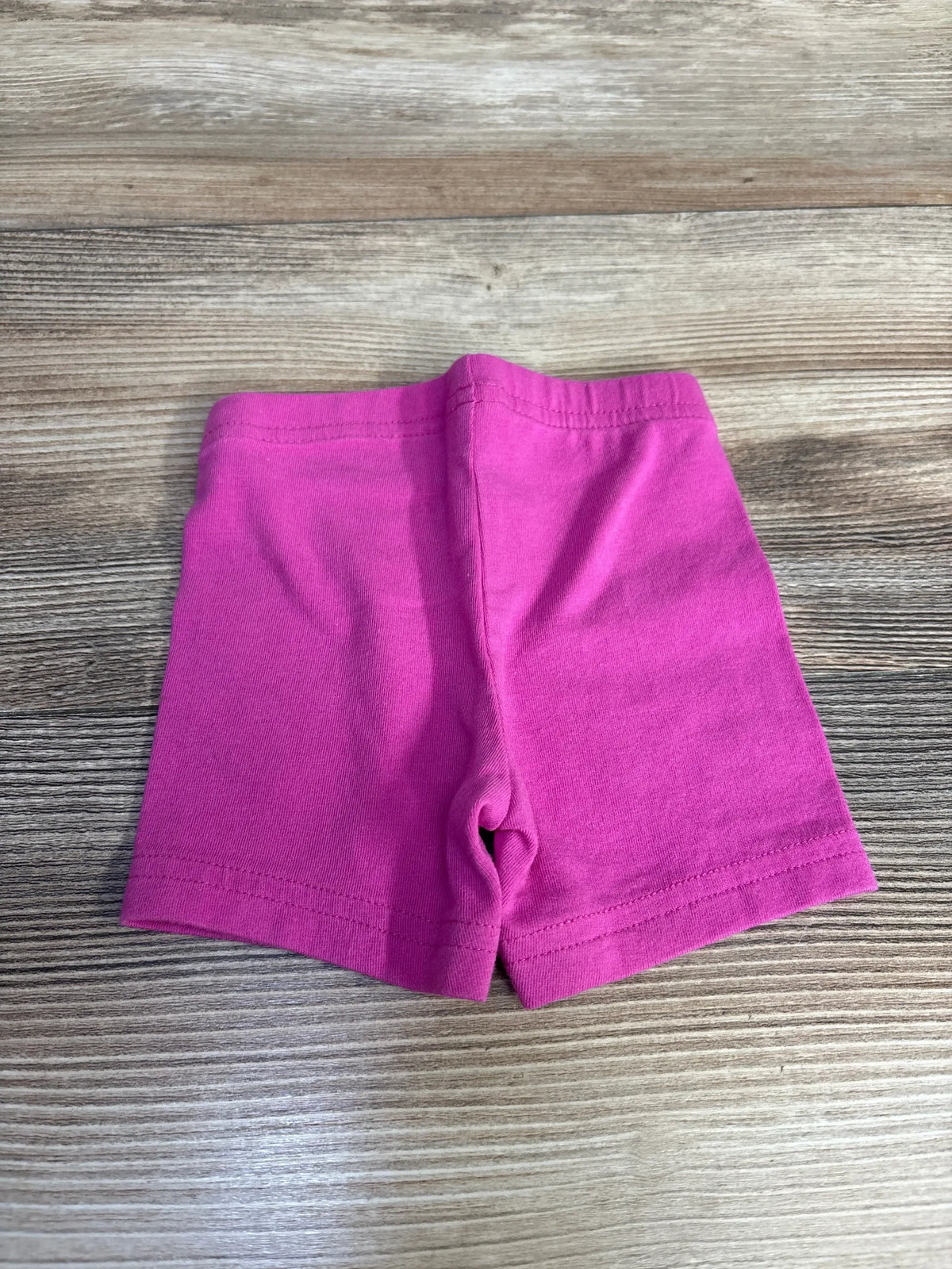 Flat lay of pink Just One You baby bike shorts size 3M showing elastic waistband and double stitched hem on wood background