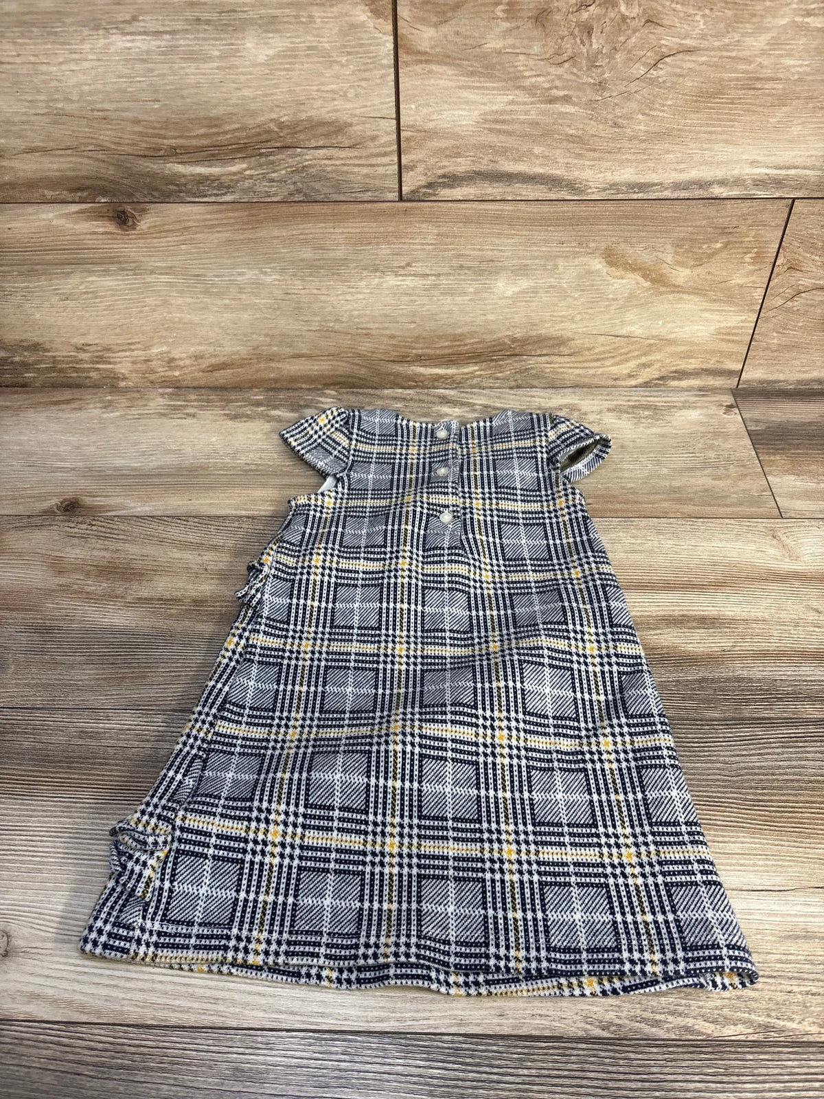 Flat-lay view of Janie and Jack plaid ruffle dress in navy, showcasing cap sleeves and ruffle details on a wood-grain background