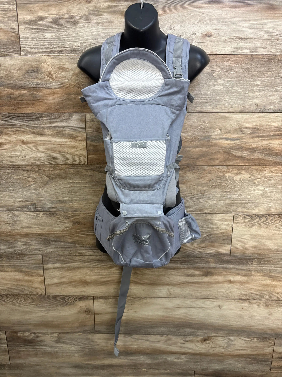 Front view of grey YSSKTC ergonomic baby carrier with hip seat and breathable mesh panels against wood flooring