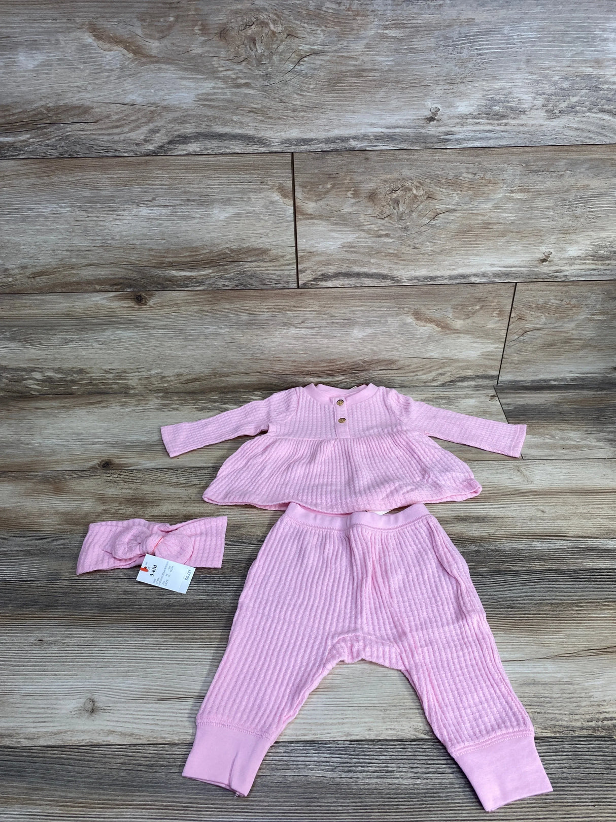 Top-down of Cat & Jack pink waffle-knit 3-piece set showing peplum top with buttons, cuffed pants, and headband on wood floor