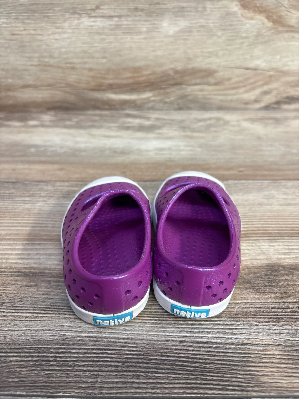 Rear of purple Native Jefferson slip-on shoes showing perforated upper, white sole, and blue native heel tag on wood surface
