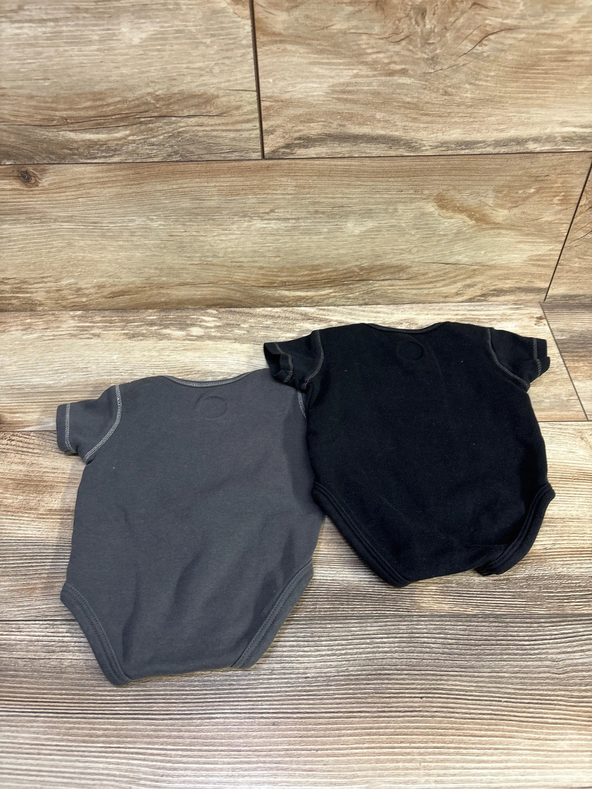 Top view of NHL Golden Knights two-pack bodysuits in gray and black, size 0 to 3 months, on a wood-look floor