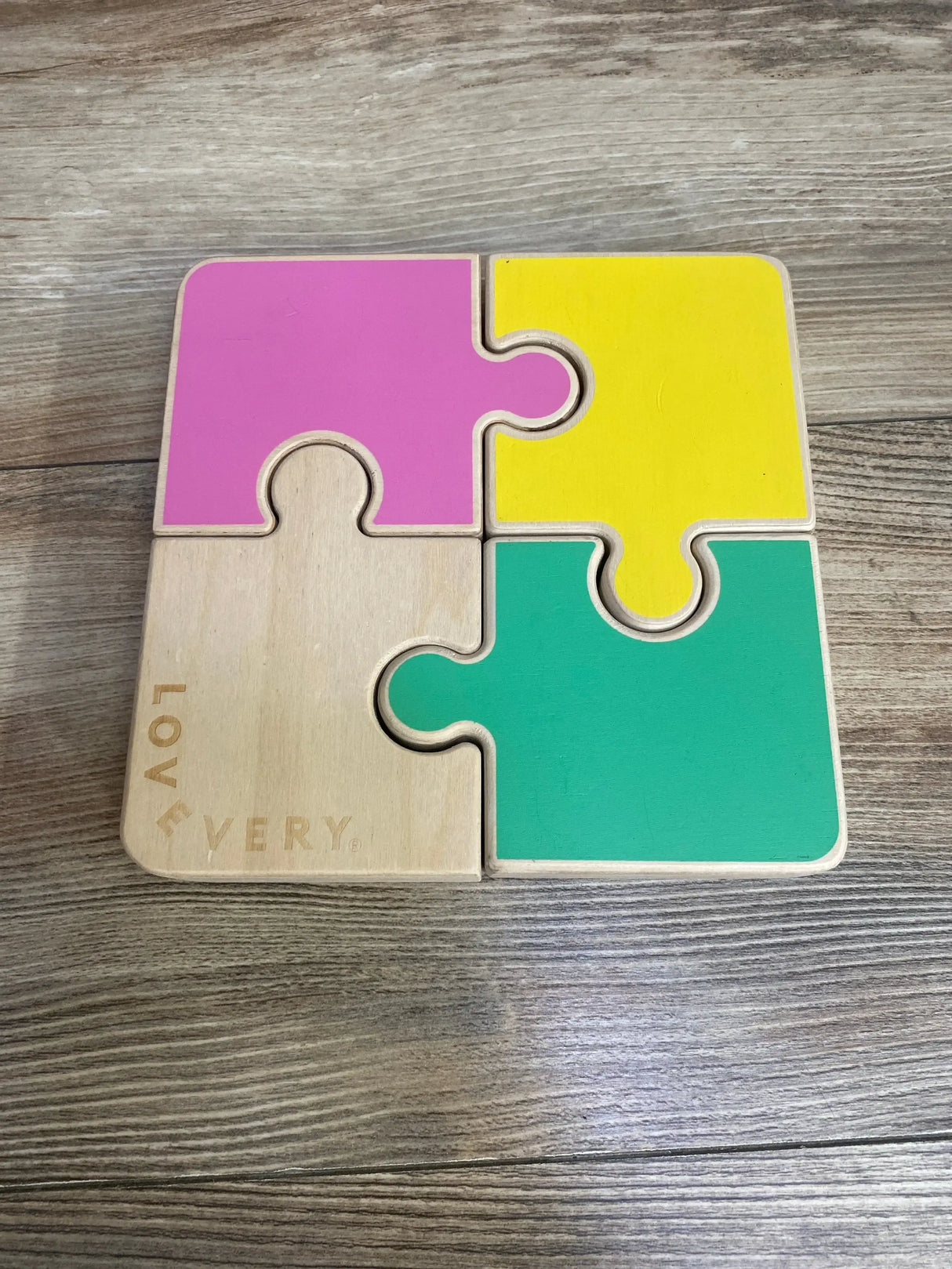 Top-down view of Lovevery Chunky Wooden Jigsaw Puzzle with four chunky pieces in pink, yellow, green and natural on wood