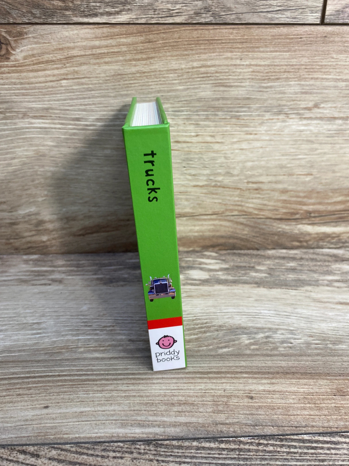 Green children's book titled 'trucks' with a truck illustration and Priddy Books logo on wooden surface