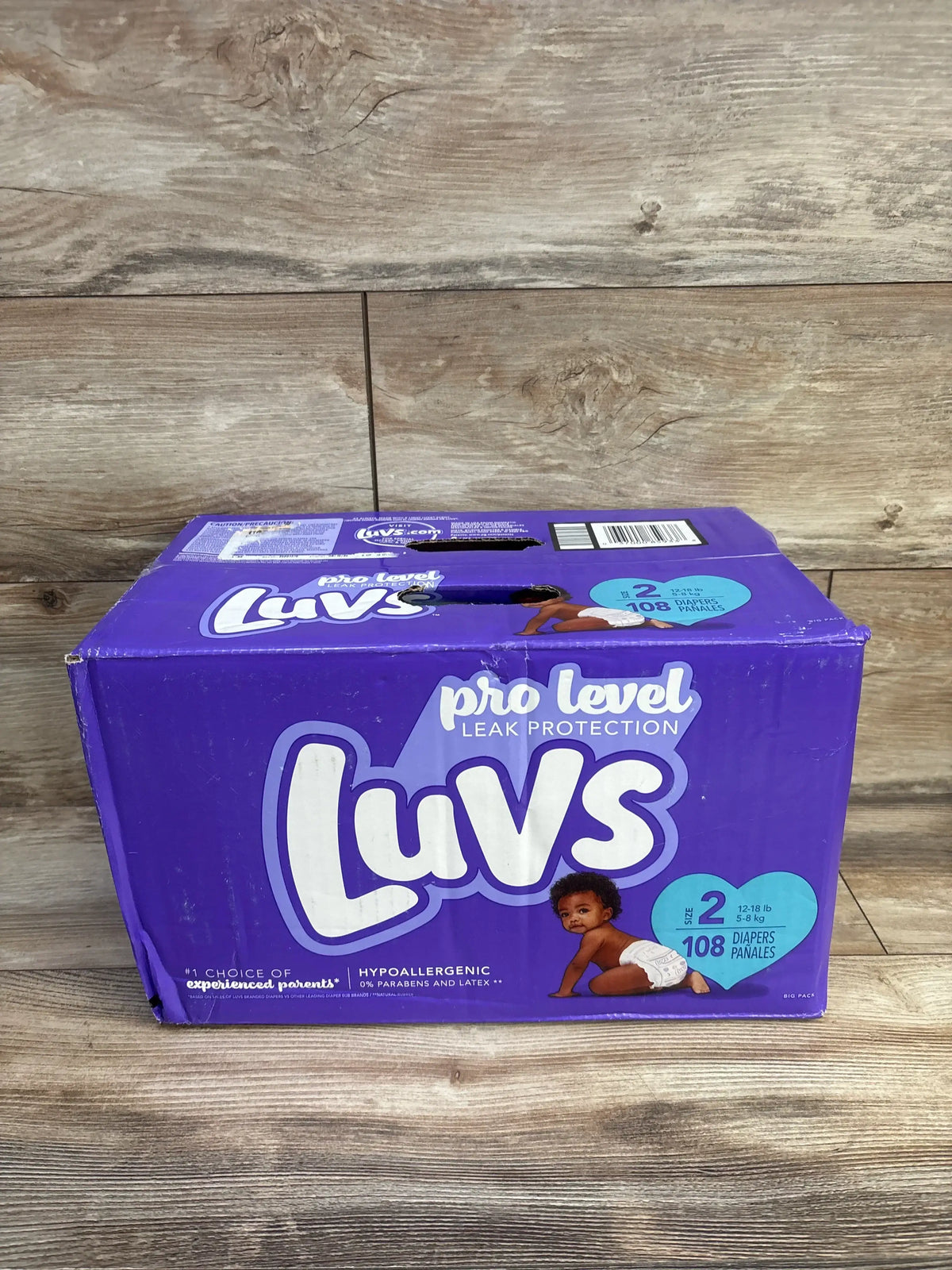 Front view of NEW Luvs diapers 108 count size 2 package showcasing leak protection on a wood floor