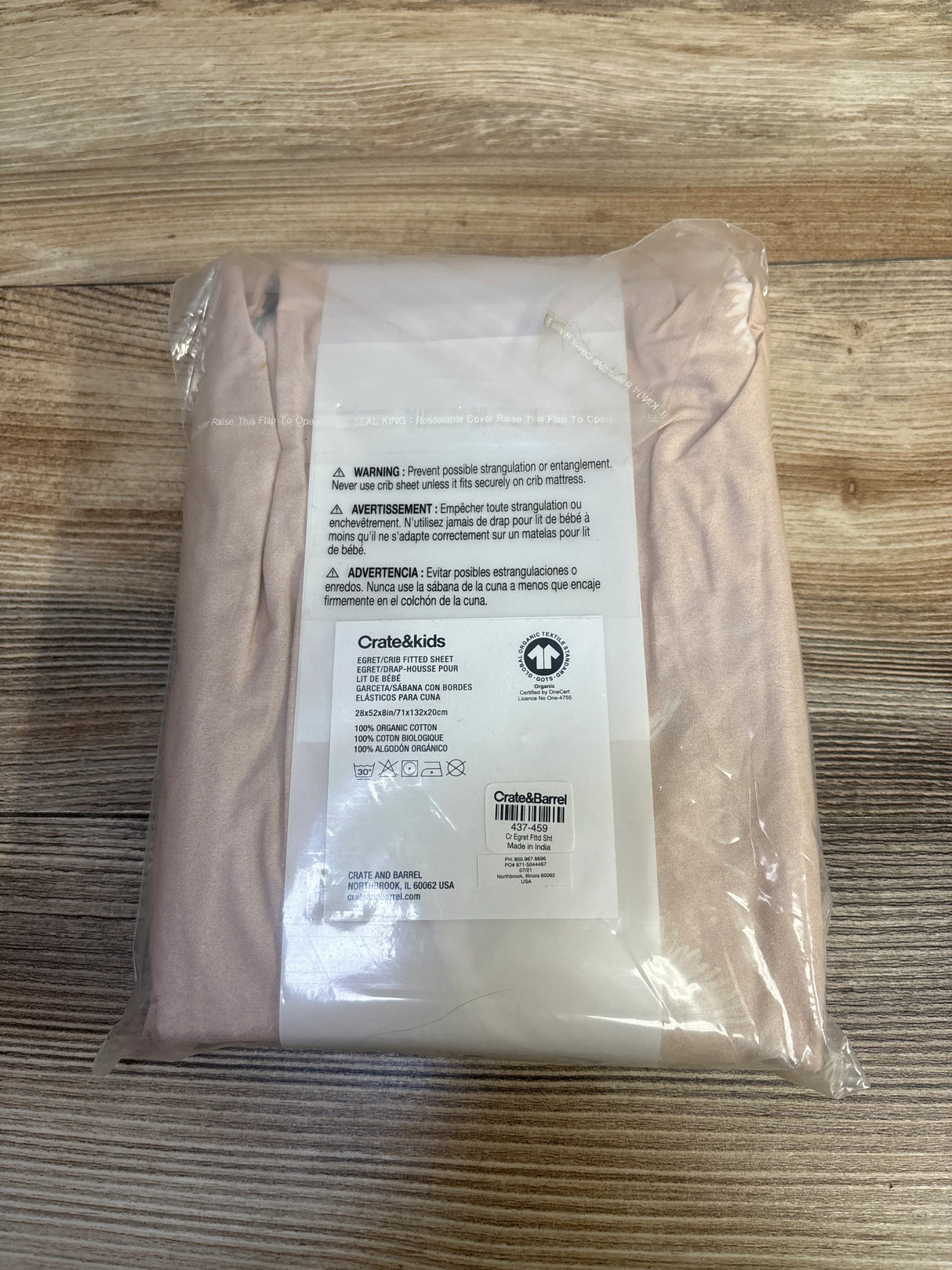 Crate&kids organic cotton crib fitted sheet in light pink, sealed in plastic packaging on wood surface