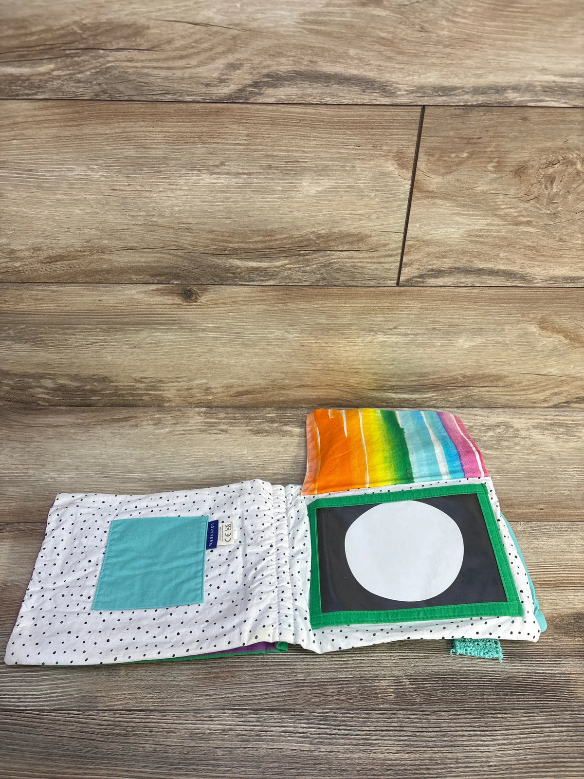 Open view of Lovevery Soft Book showcasing tactile black and white and colorful fabric pages on a wood floor