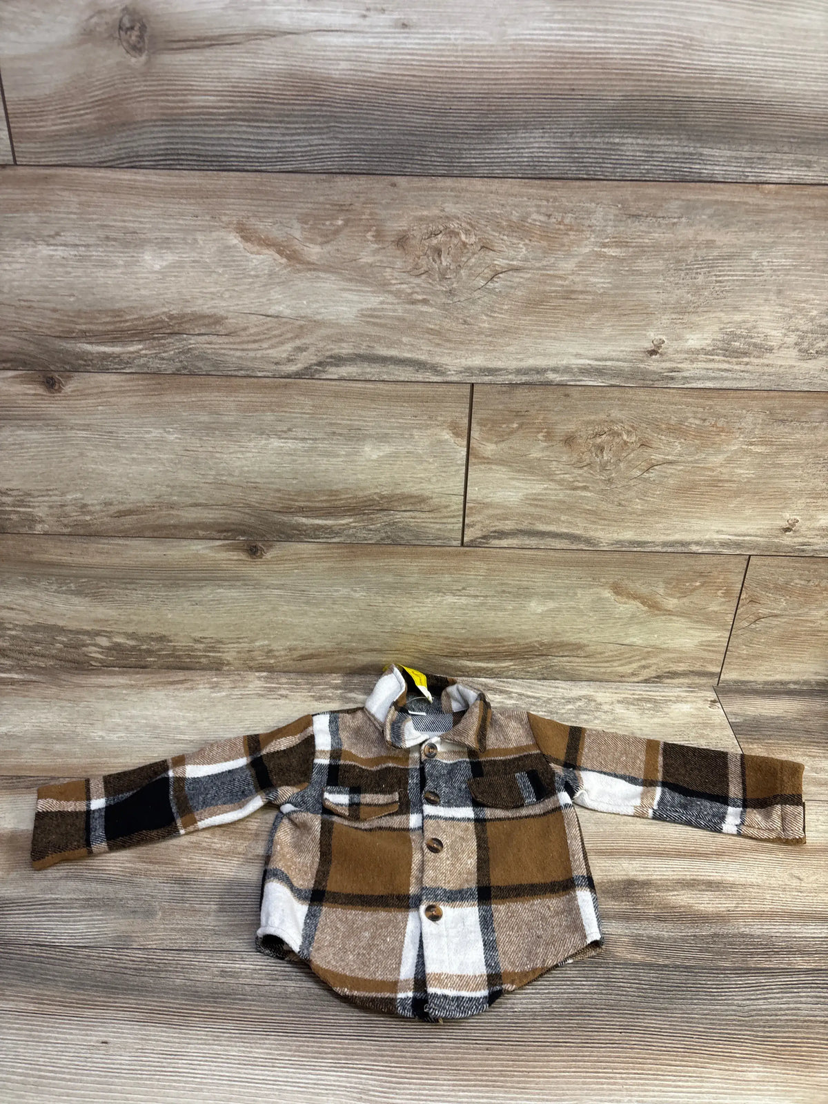 Flat lay of toddler brown and cream plaid shacket showing front buttons and chest pockets on wood floor background