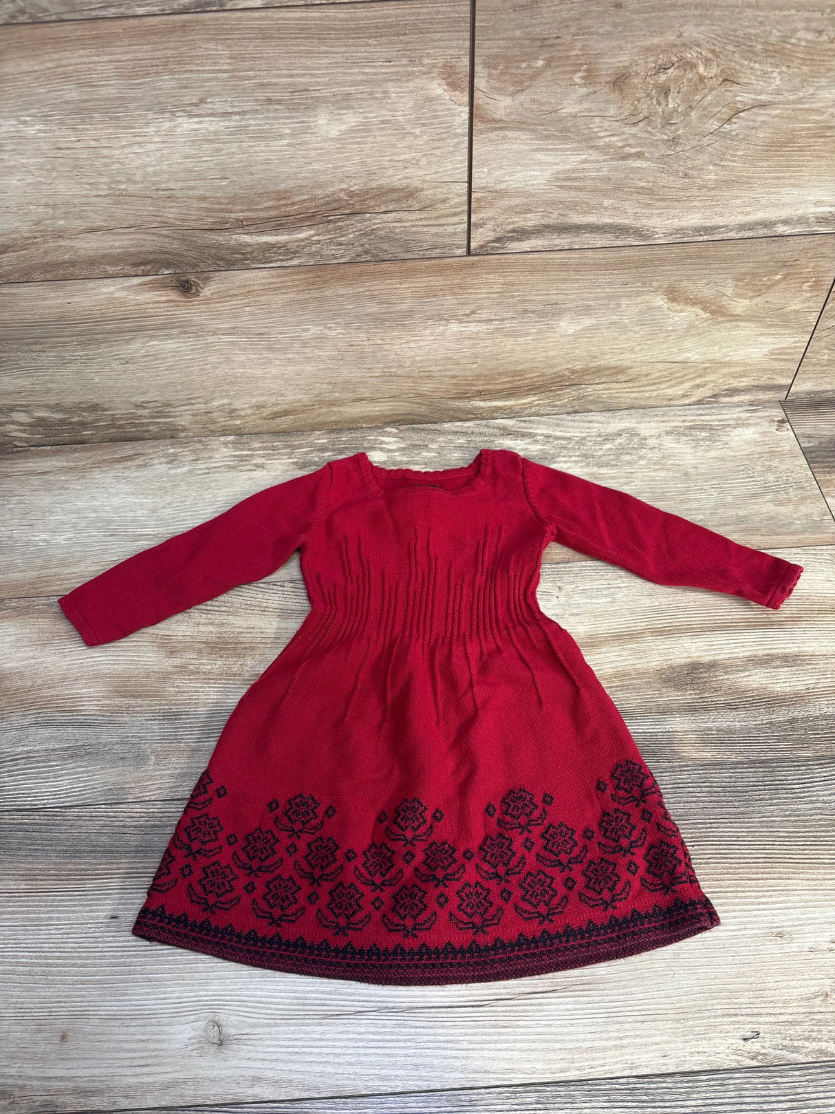 Red long sleeve toddler dress with black floral embroidery on skirt, laid flat on wooden floor