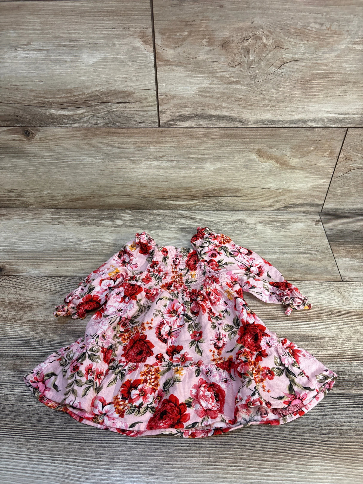 Flat lay of Old Navy newborn pink smocked fit-and-flare dress showing smocked bodice and red floral print on wood floor