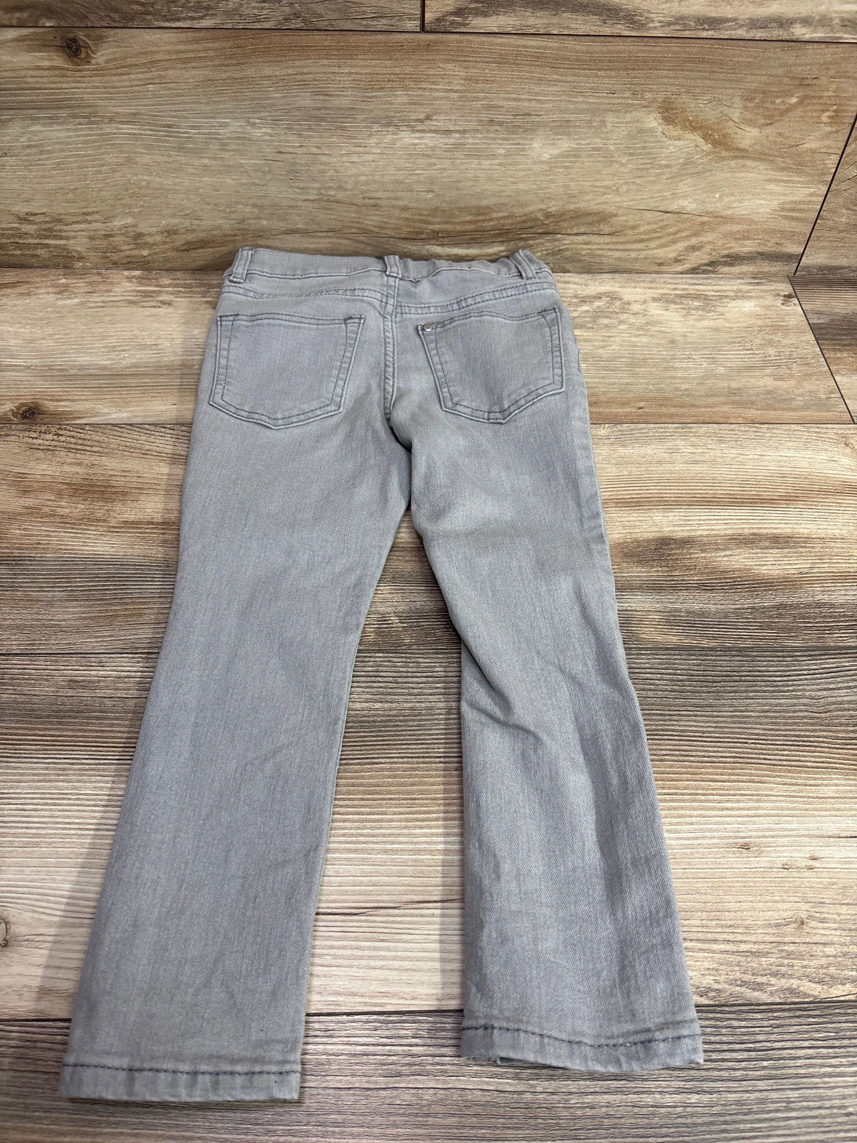 Back view of grey H&M denim skinny jeans for toddlers size 4T on a wooden background.