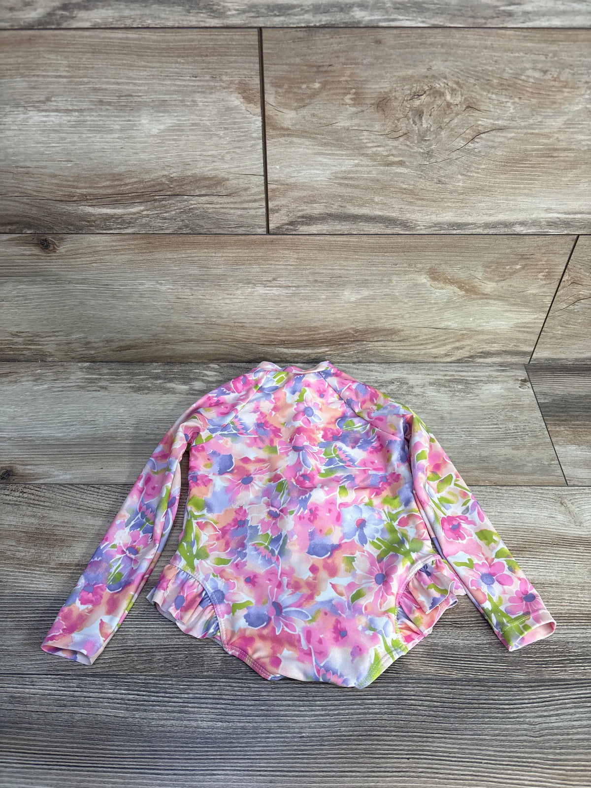 Front view of Banana Boat 1pc long sleeve rash guard swimsuit in pink, showcasing floral print on wood-grain background