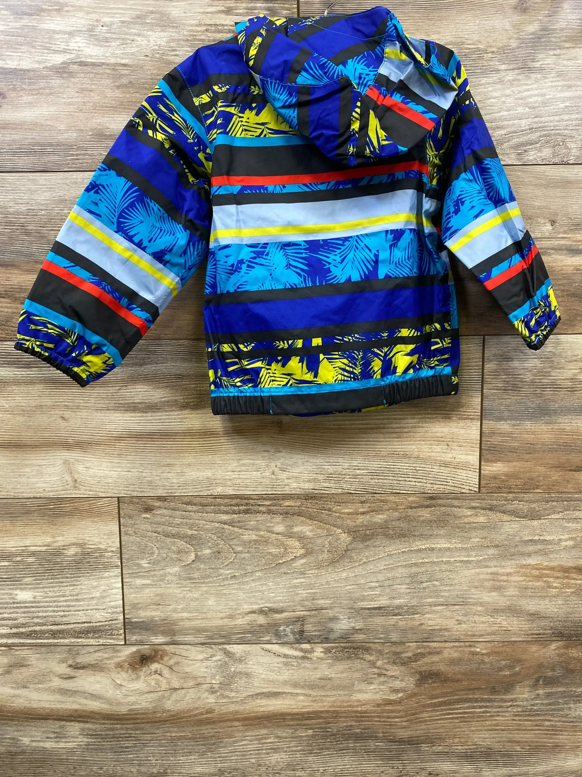 Front view of The North Face Tailout toddler rain jacket, blue with yellow and black stripes and palm leaf print, hooded, on wooden floor