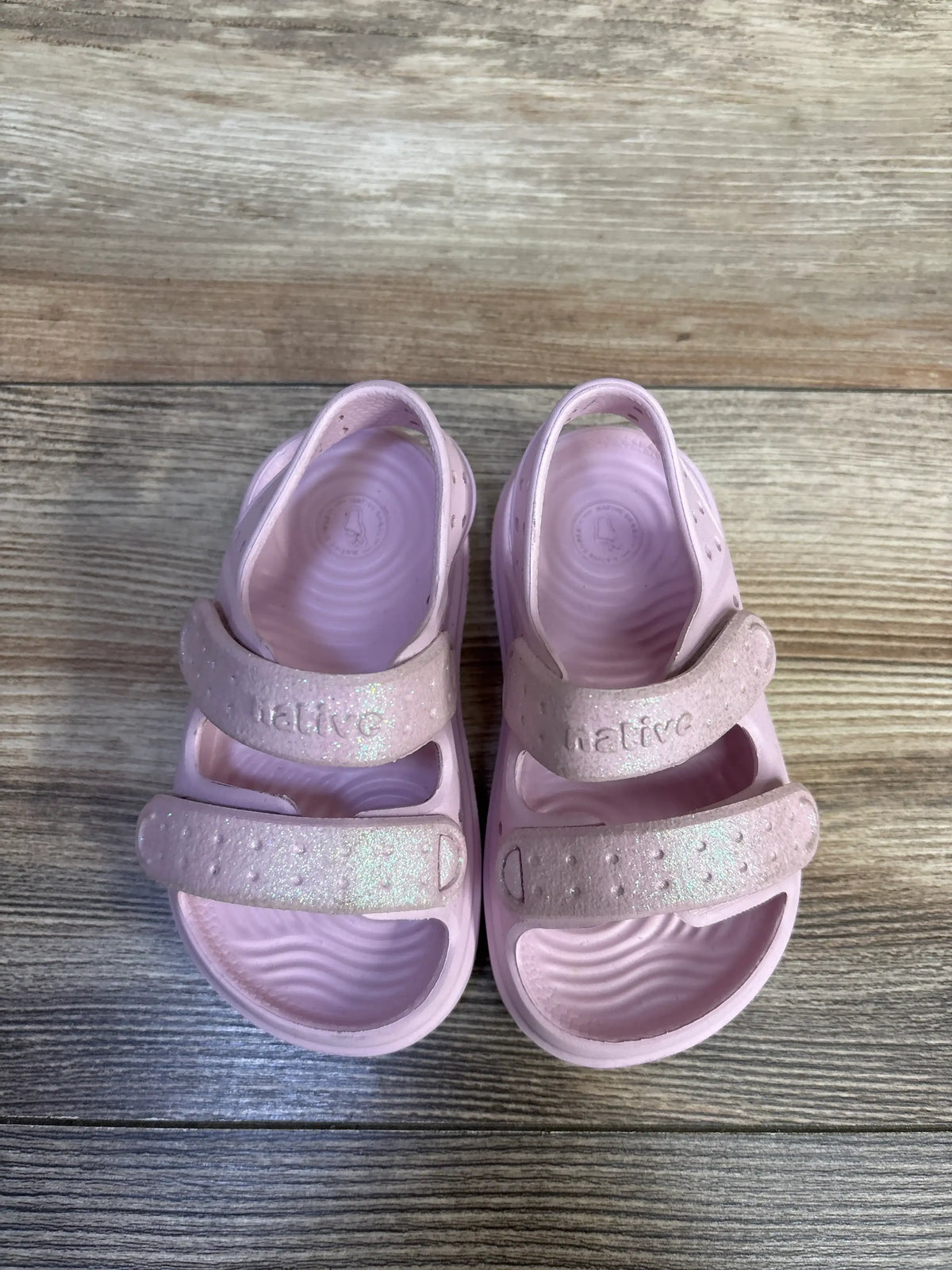 Pink Native Chase Bio-Bling sandals for kids with glittery straps on a wooden surface