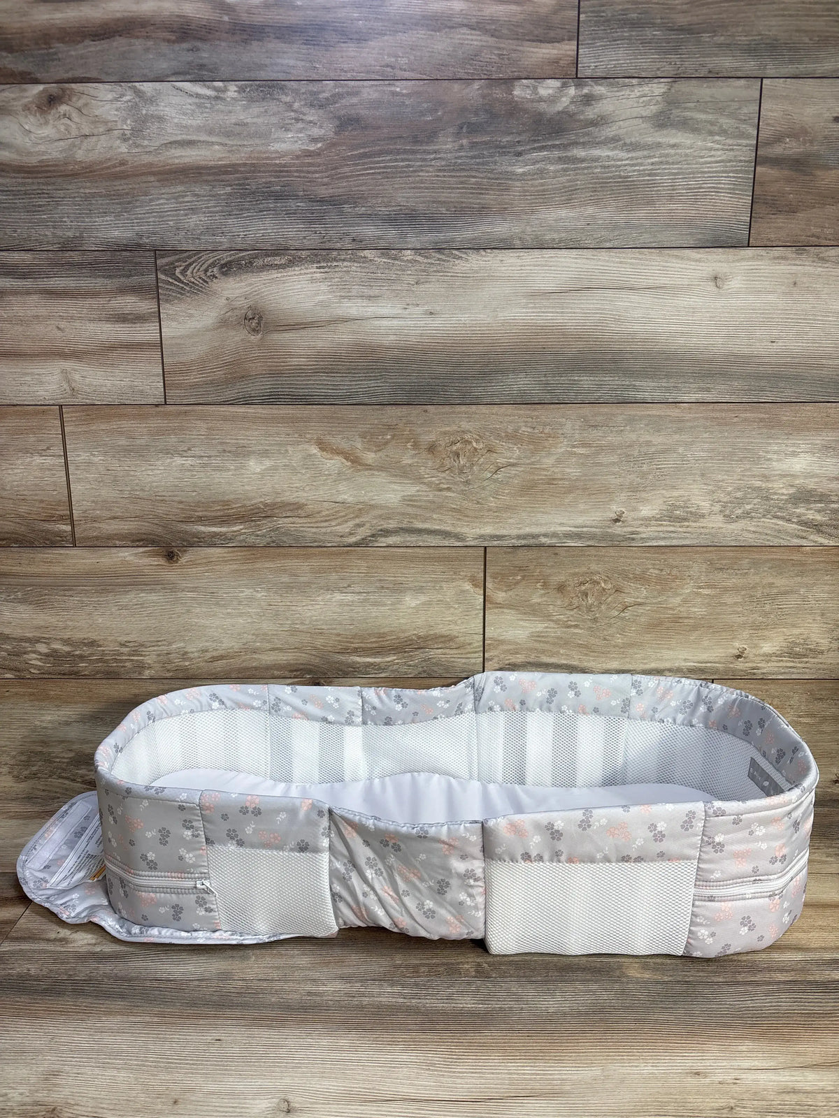 Front view of Baby Delight Snuggle Nest infant lounger with gray floral print, mesh sides and exterior pockets on wood floor