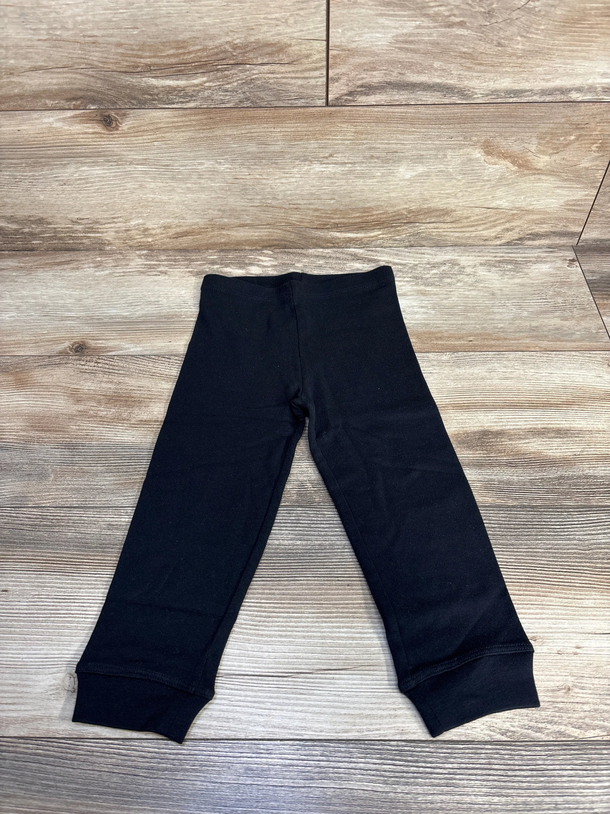 Black baby leggings with cuffed ankles laid flat on wood grain floor